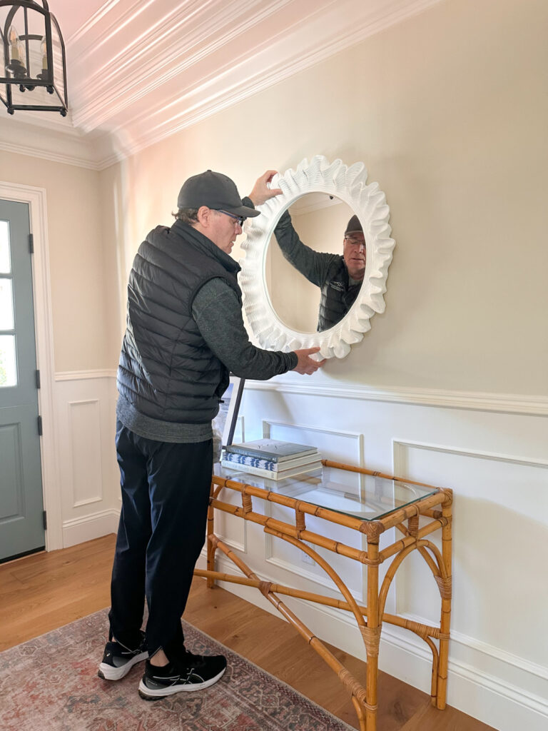Man holding mirror up to wall before hanging it.