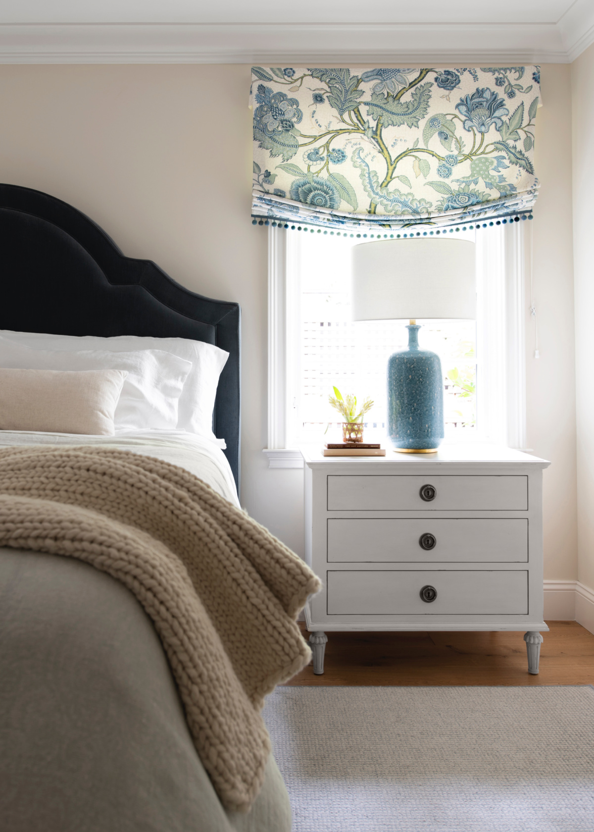 Main bedroom with blue velvet headboard, nightstand and lamp.