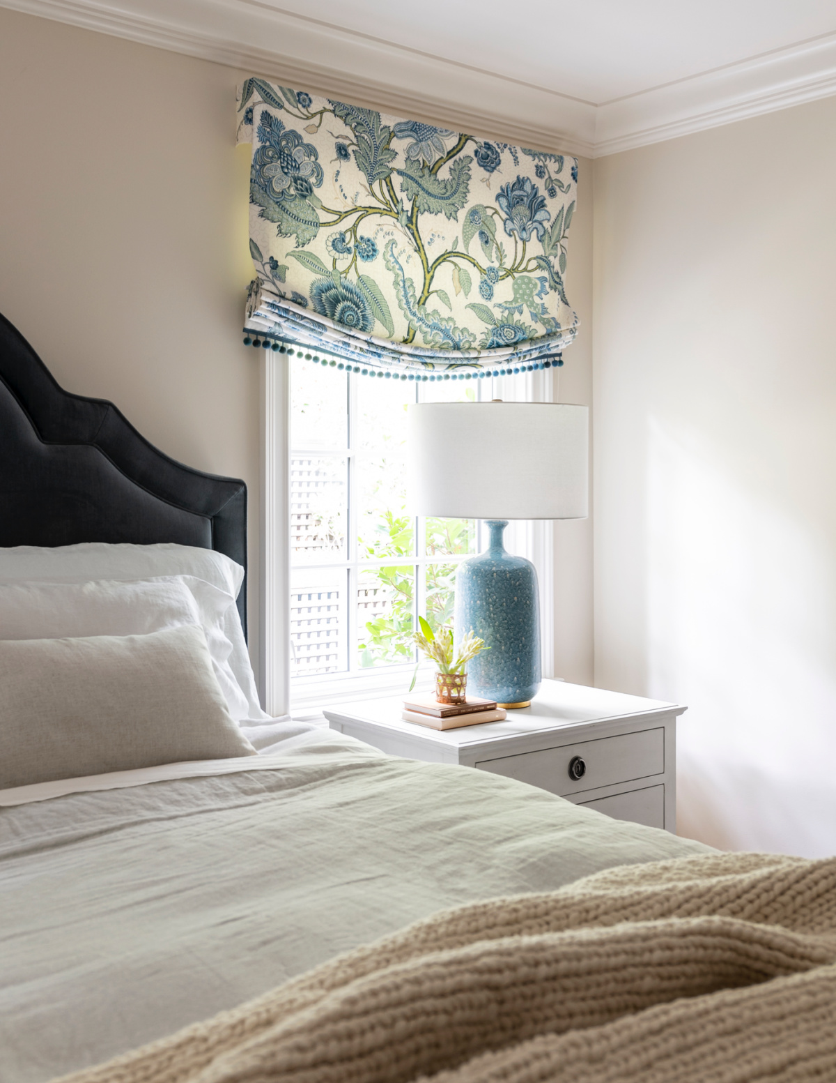 Bedroom with blue velvet headboard and colorful roman shade.