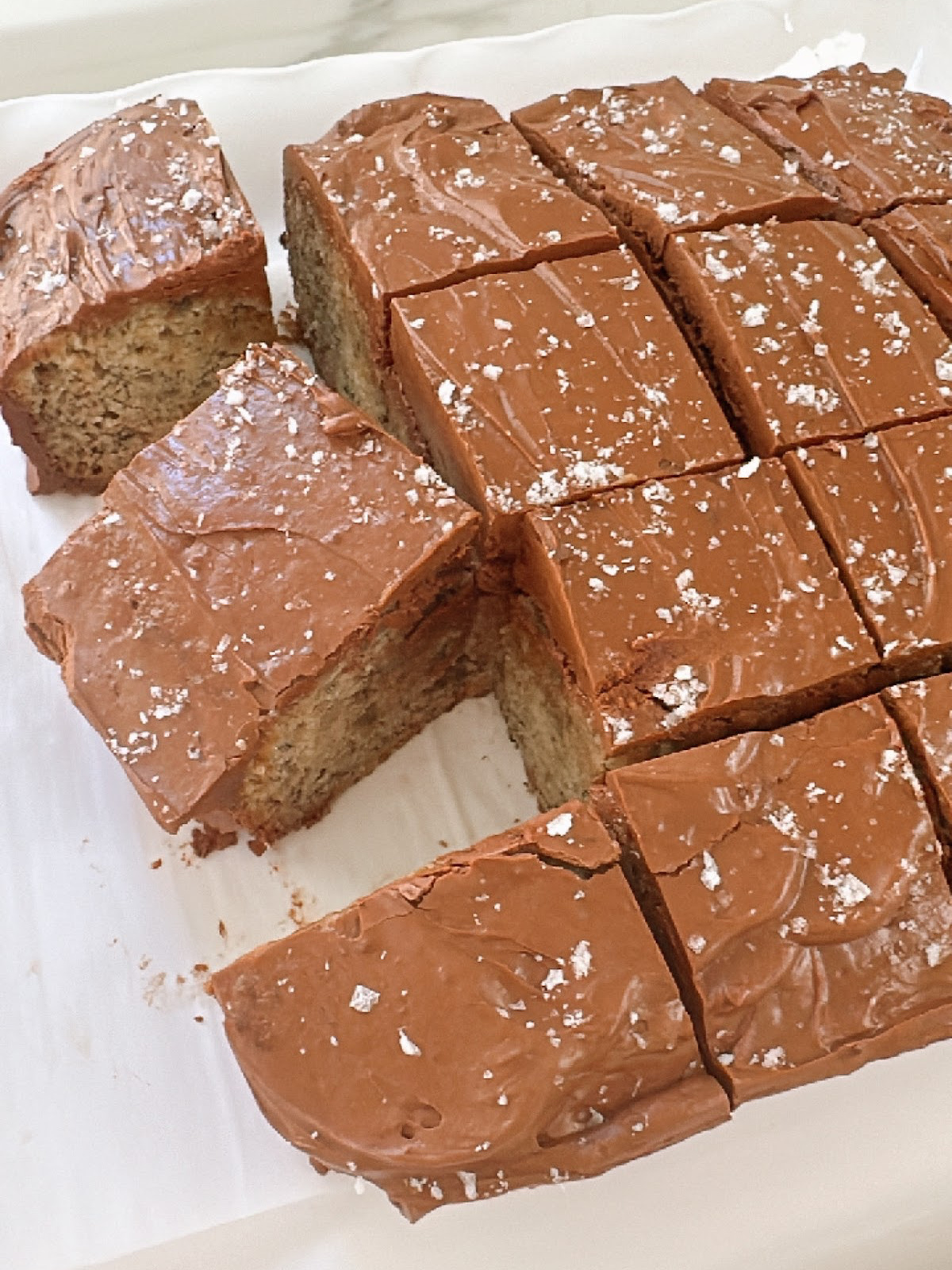 Sliced pieces of banana cake with chocolate frosting sprinkled with sea salt.