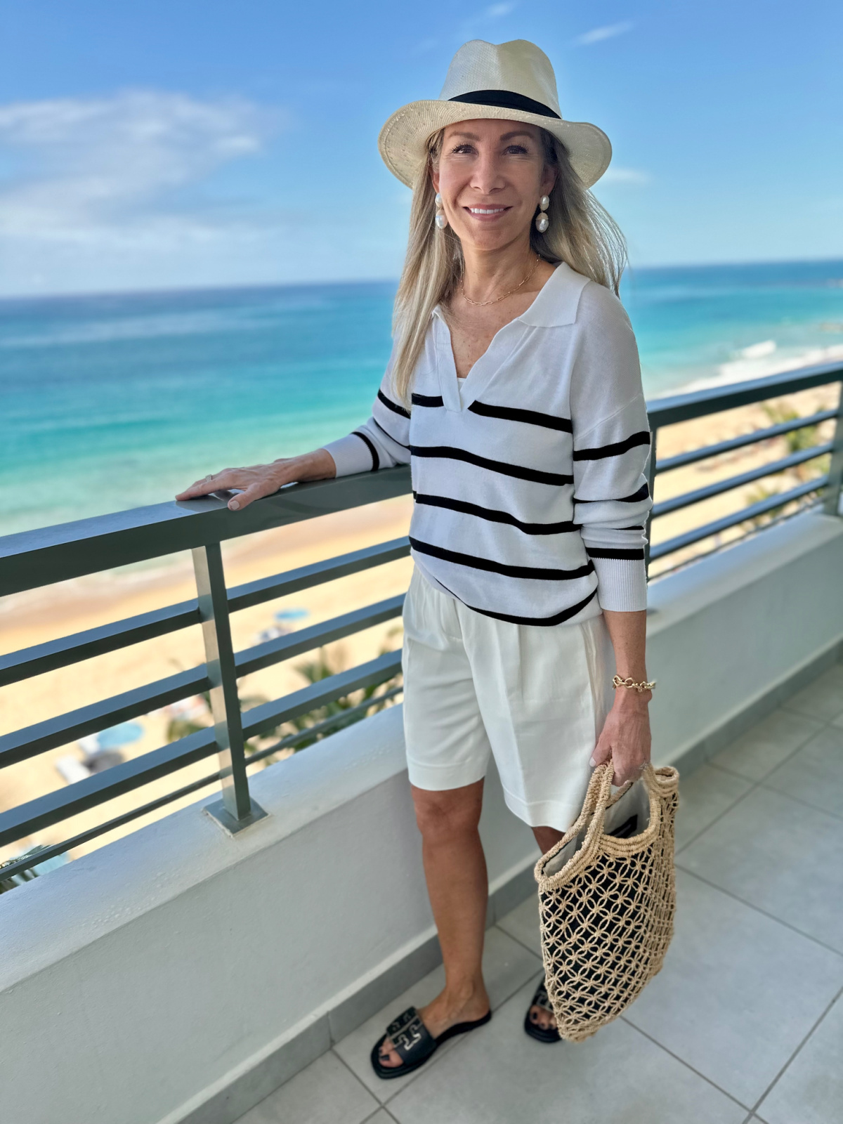 Woman standing on balcony overlooking Atlantic oceans wearing striped sweater and shorts.