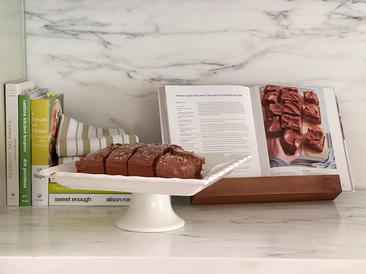 Cookbooks on counter, one open on stand, and cake plate with slices pieces of cake.