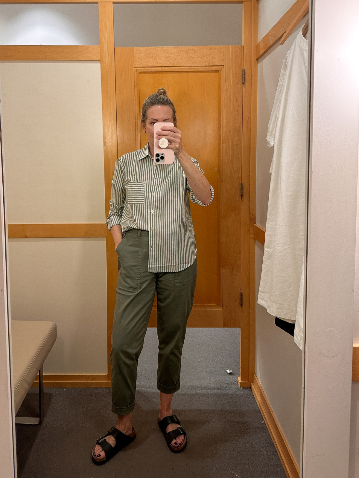Woman taking mirror selfie in dressing room trying on striped shirt.