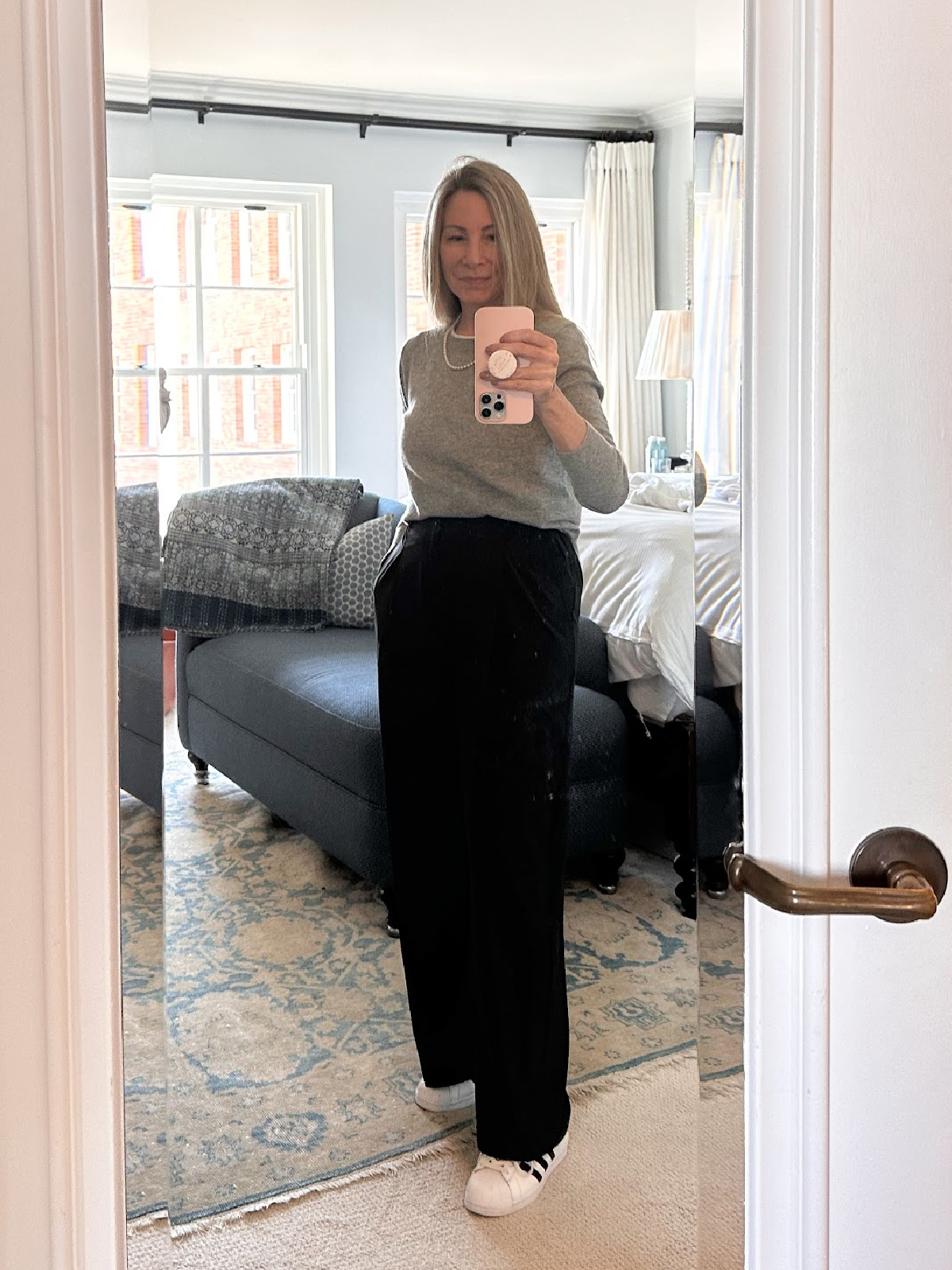 Woman taking mirror selfie in hotel room wearing Adidas Superstars.