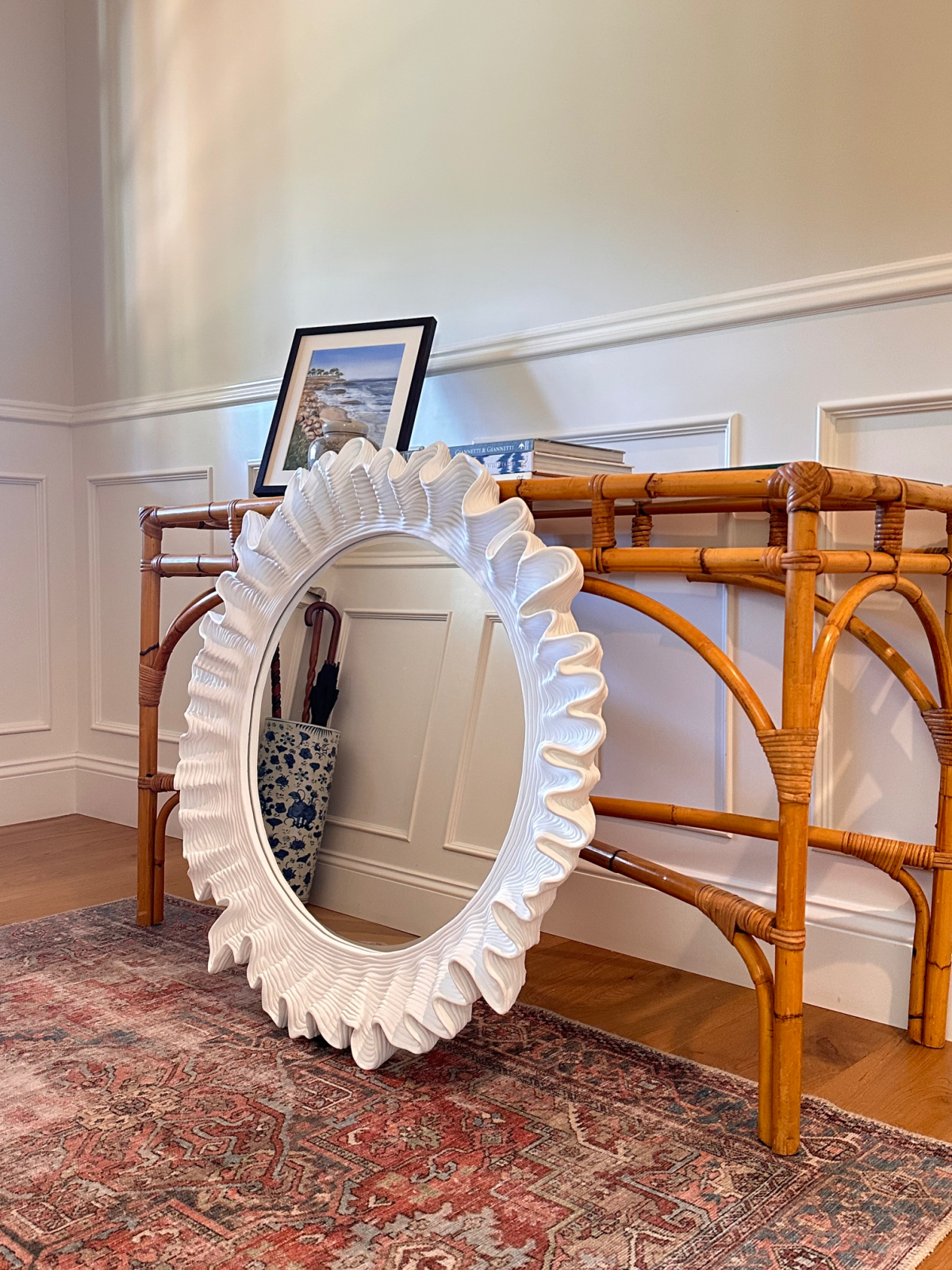 Round, scalloped mirror leaning against bamboo table.