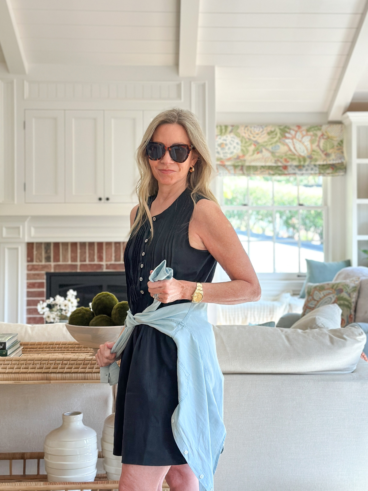Woman wearing sunglasses and Quince linen dress tying chambray shirt around waist.