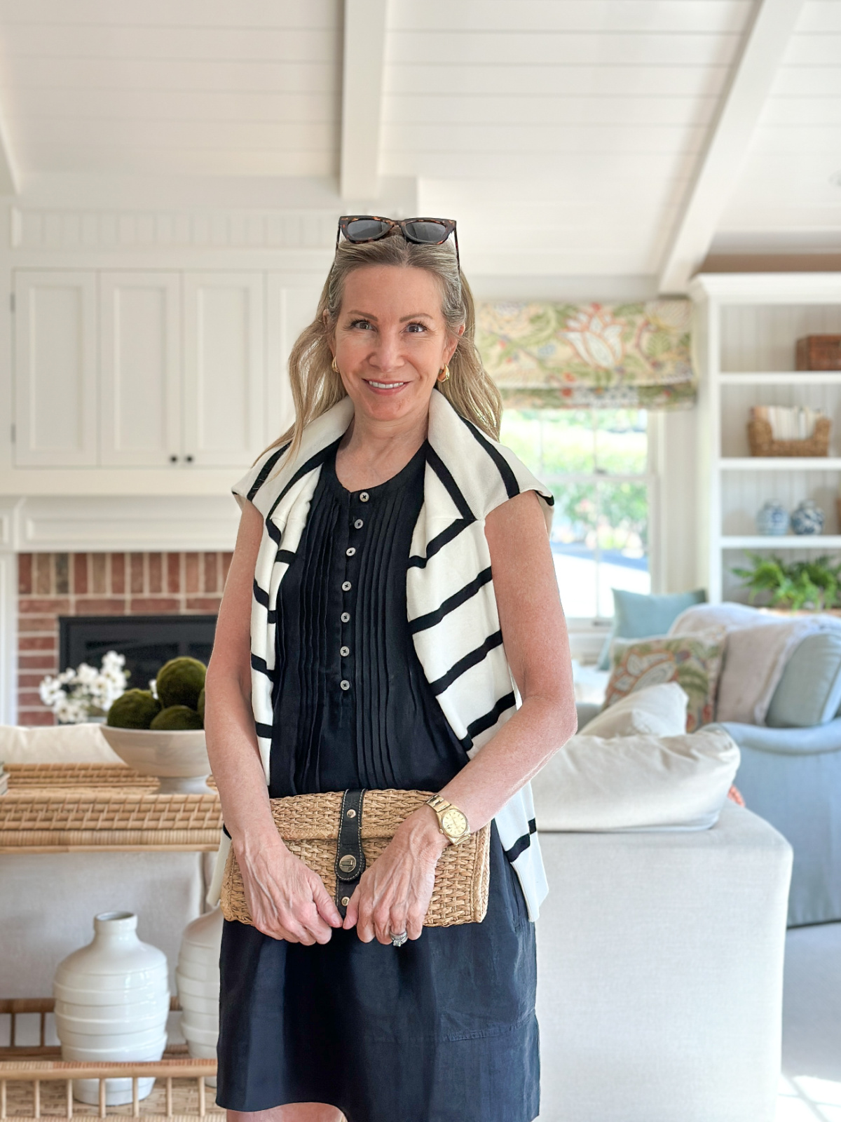 Woman wearing Quince linen dress with black and white sweater over shoulders and Kate Spade clutch.