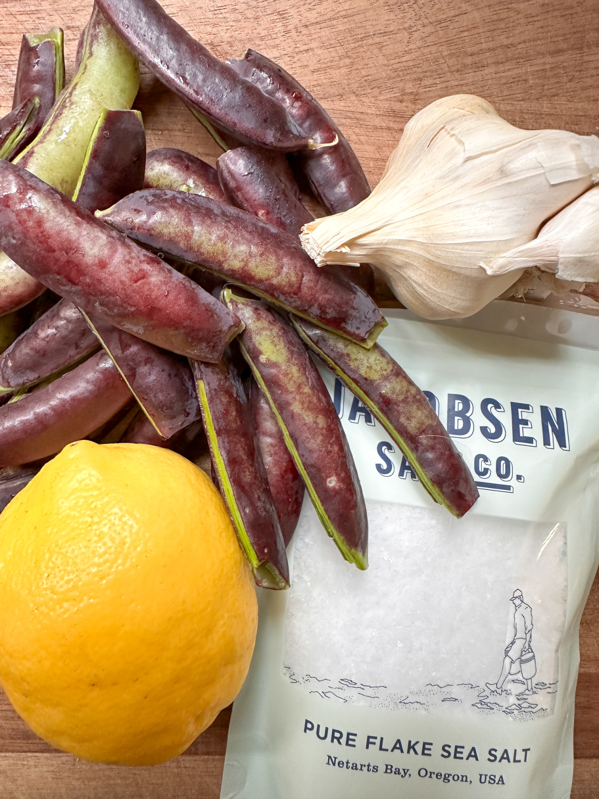 Snap peas, garlic, salt and a lemon on cutting board.