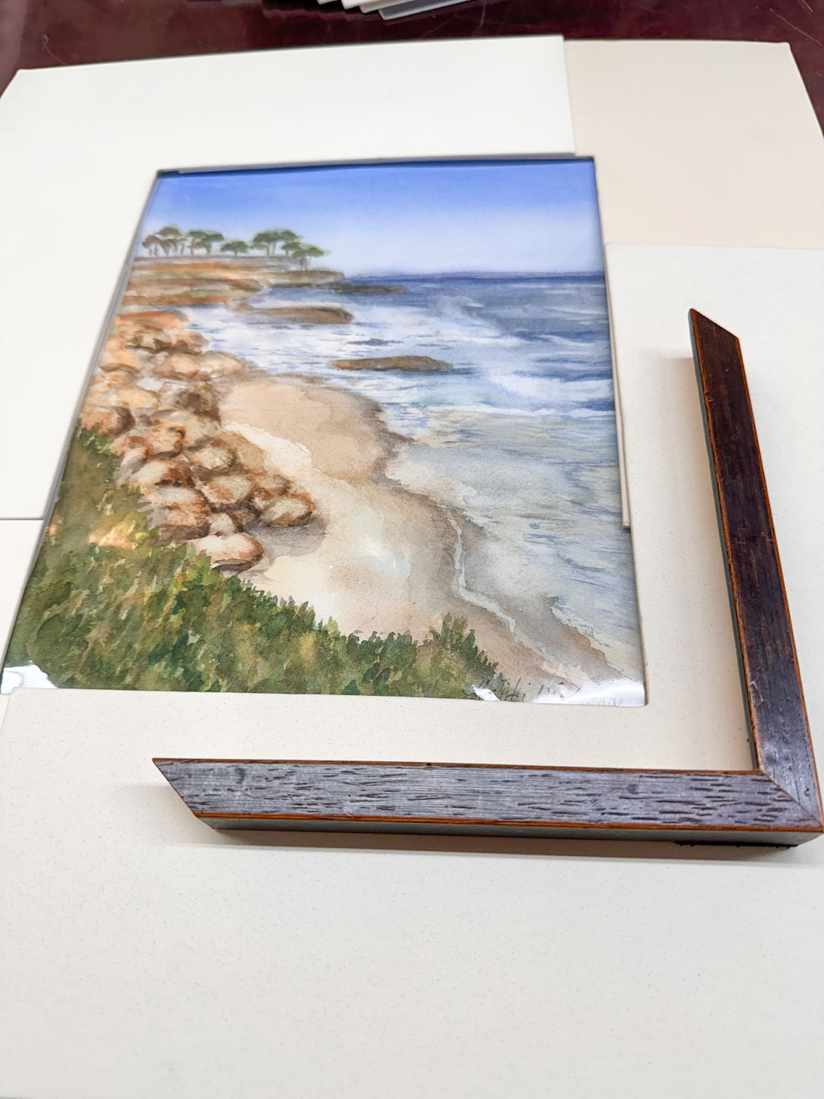 Coastal watercolor laying next to map and corner frame.