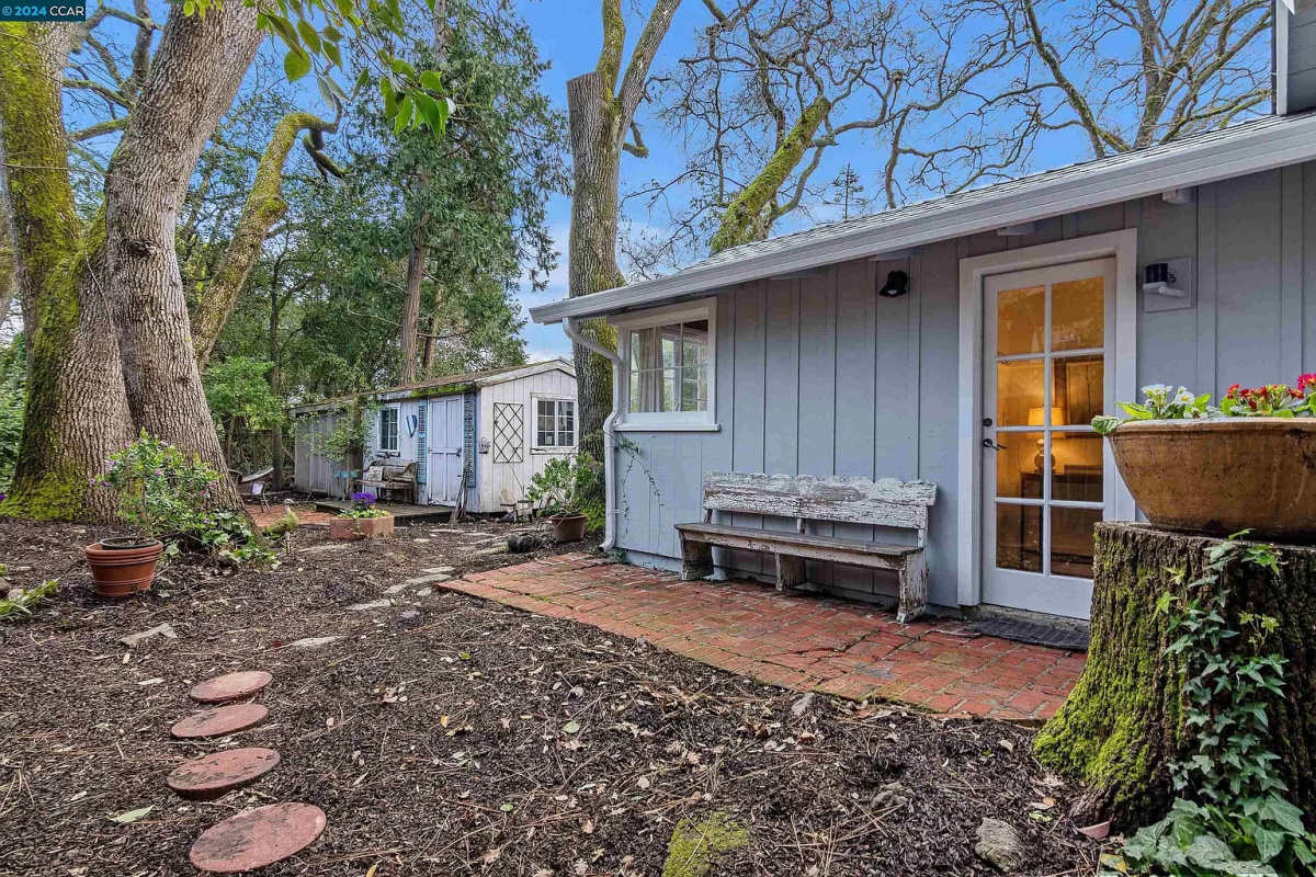 Tiny blue cottage from the back with vintage bench on brick patio.