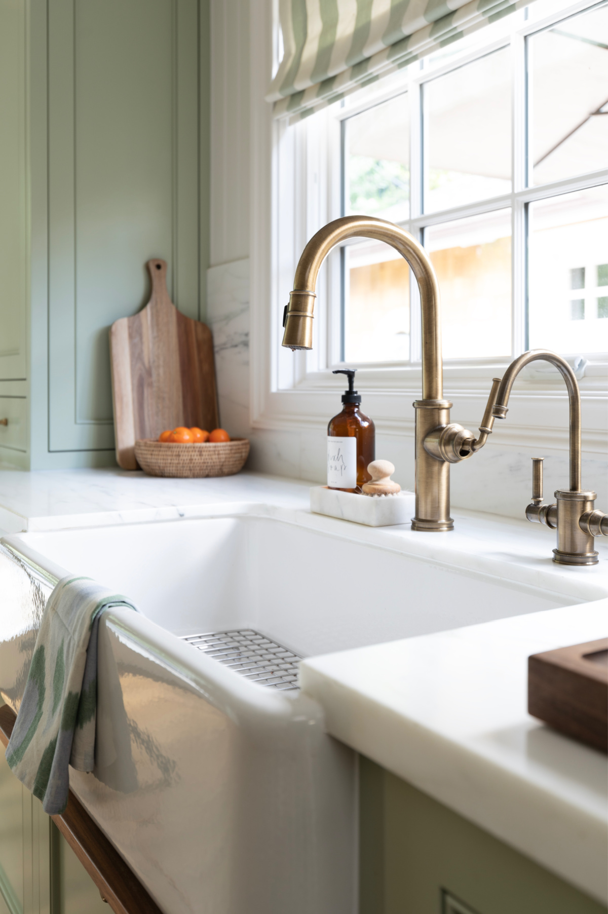 Farm sink and brass fixtures in green kitchen.