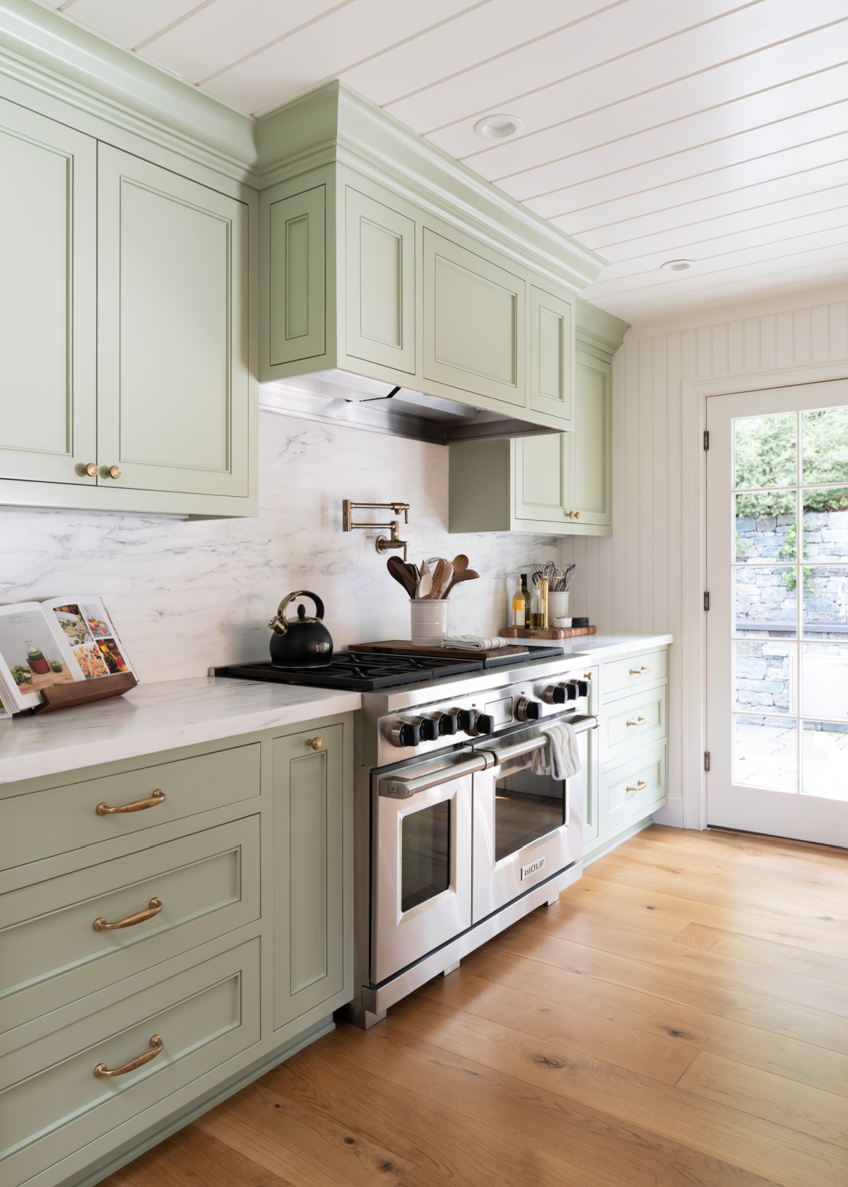 Left side of galley kitchen with green cabinets and Wolf range.