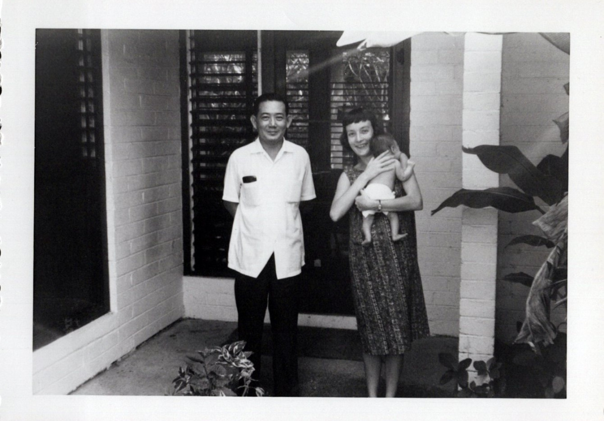 Man and woman holding baby in front of house in the Philippines.