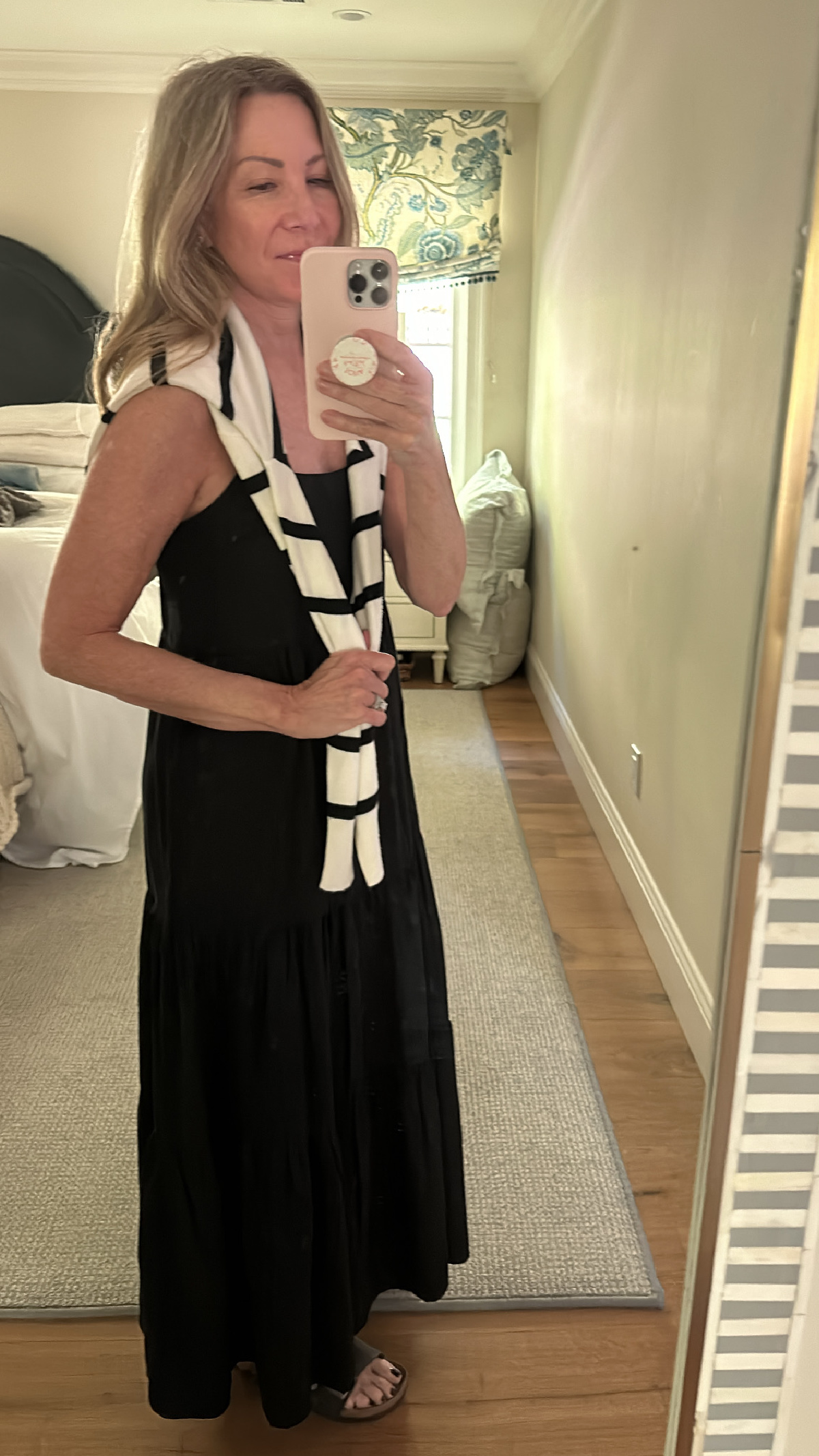 Woman taking mirror selfie wearing black dress, striped sweater over shoulders and Birkenstocks.