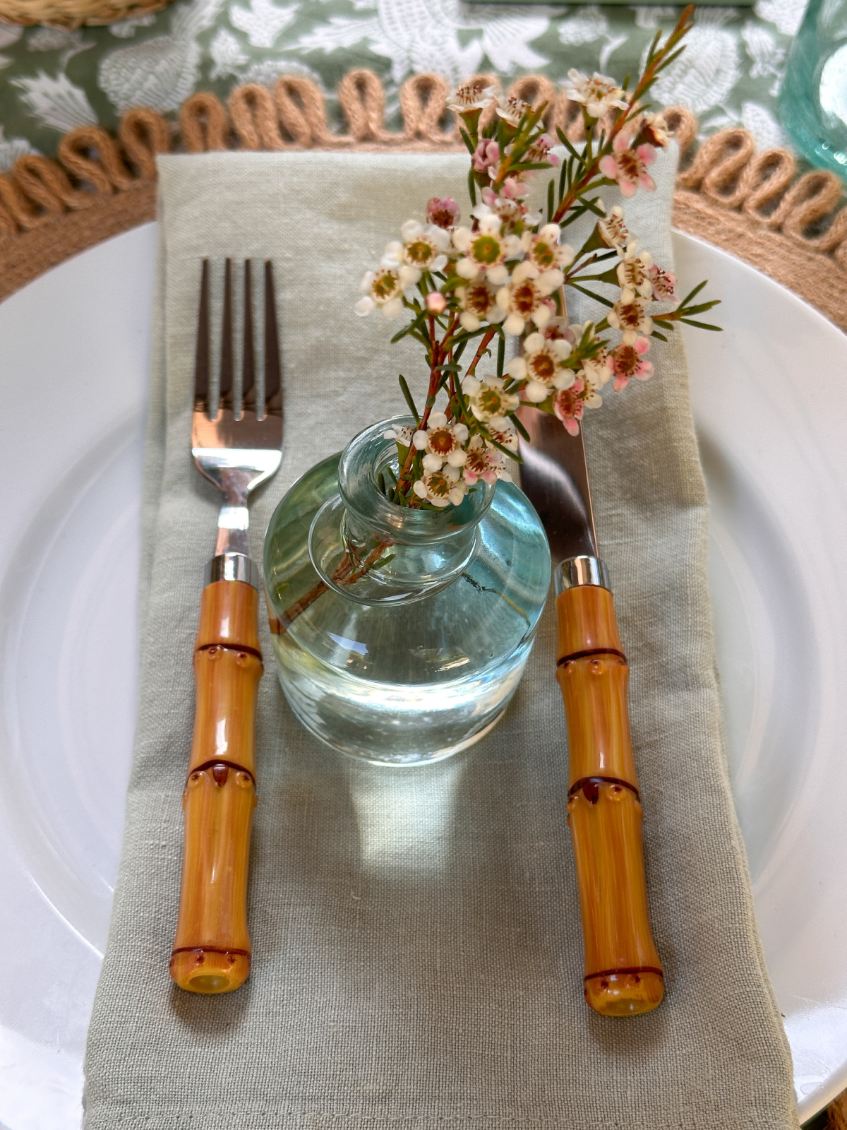 Overhead shot of placesetting with napkin, bud vase and bamboo knife and fork on white plate.