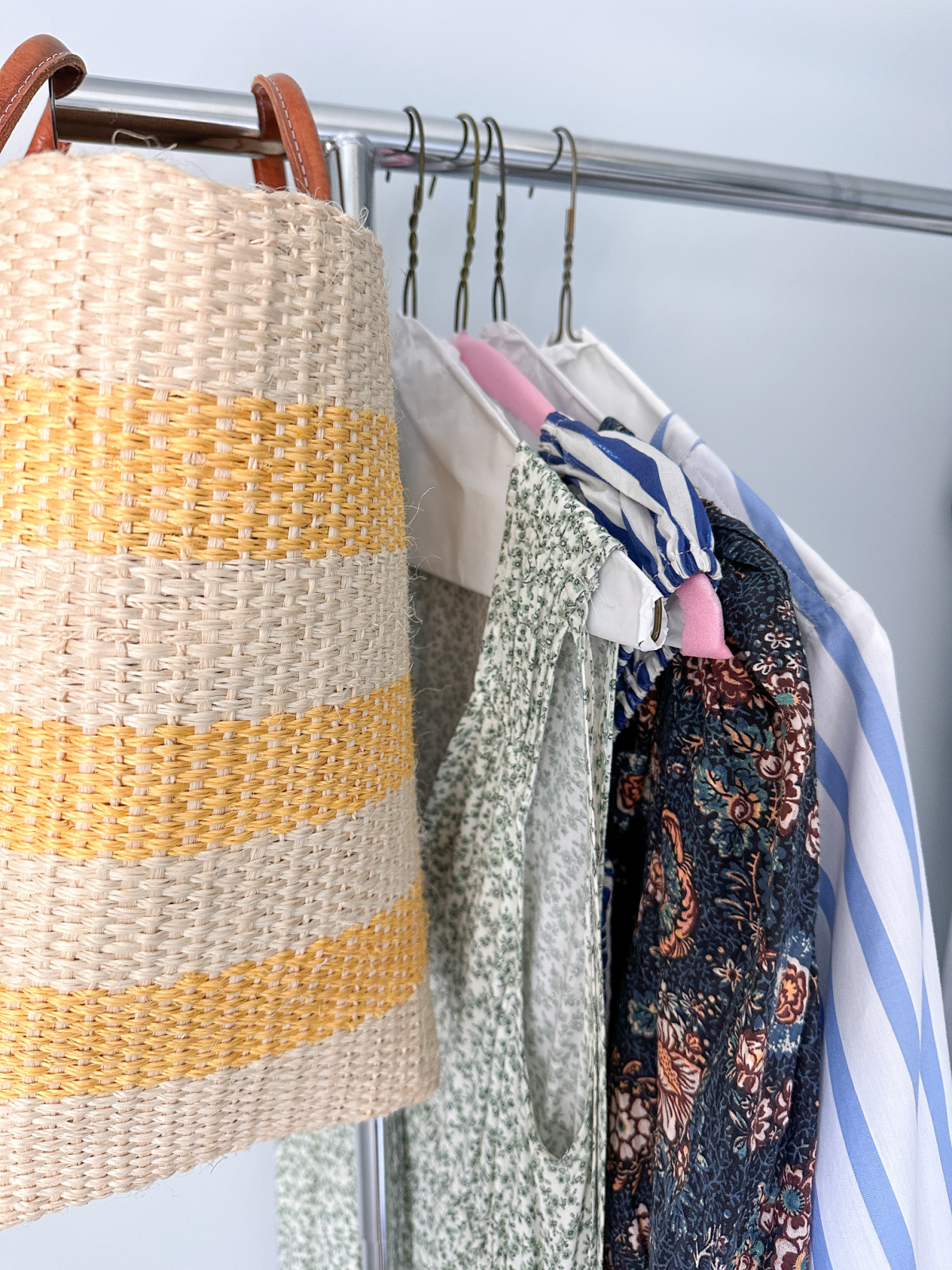 Straw tote and summer dresses hanging on rolling rack.