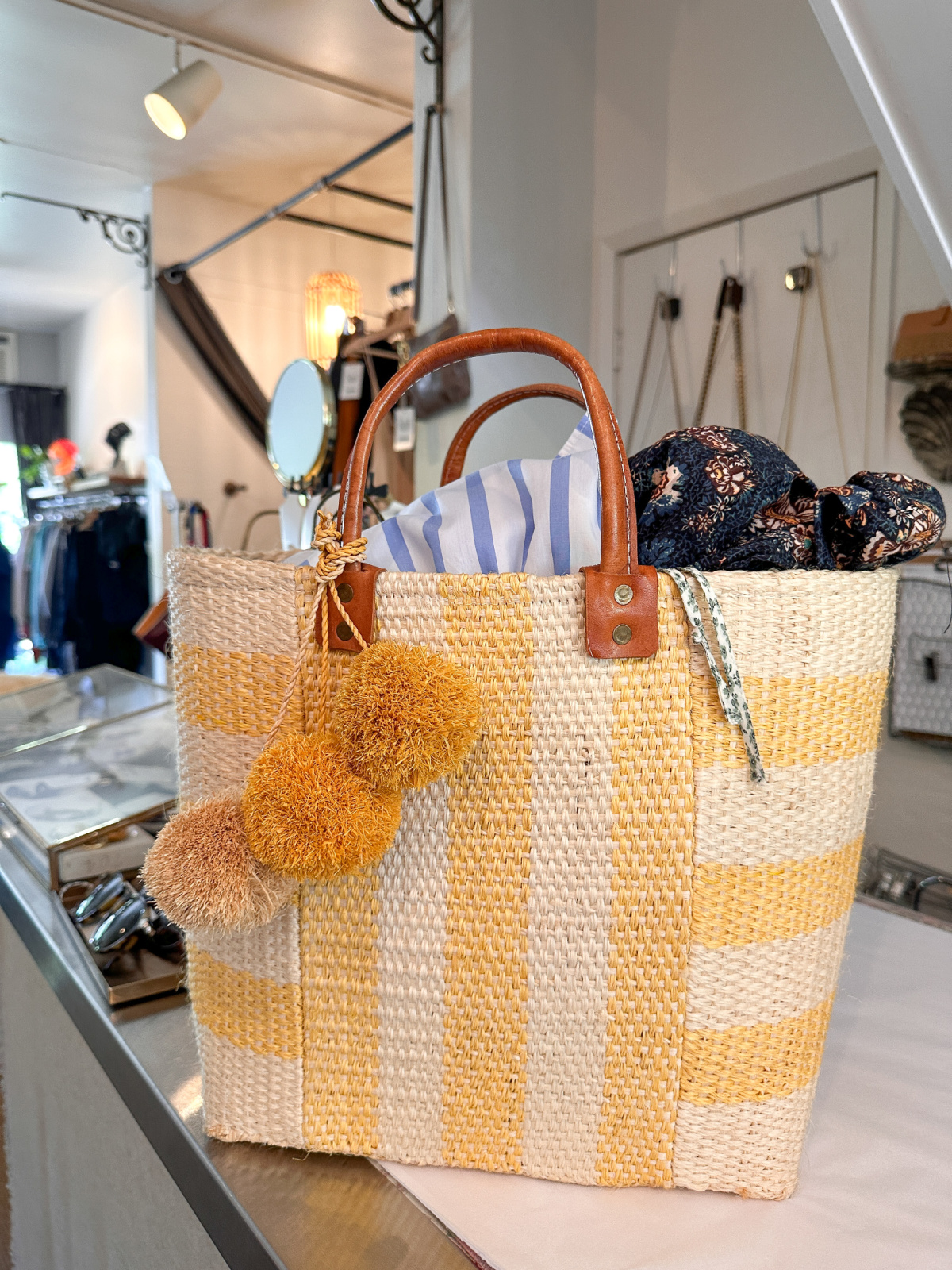 Yellow and white stripped market tote filled with summer dresses sitting on sales counter of consignment shop.