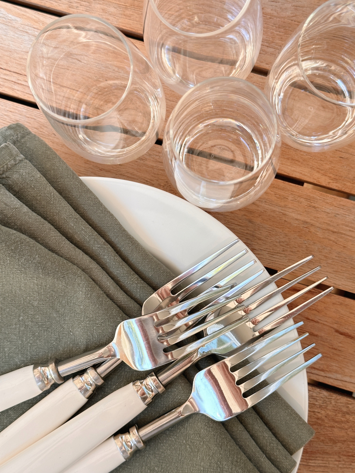 Overhead shot of white plates, green napkins, forks and stemless champagne flutes.