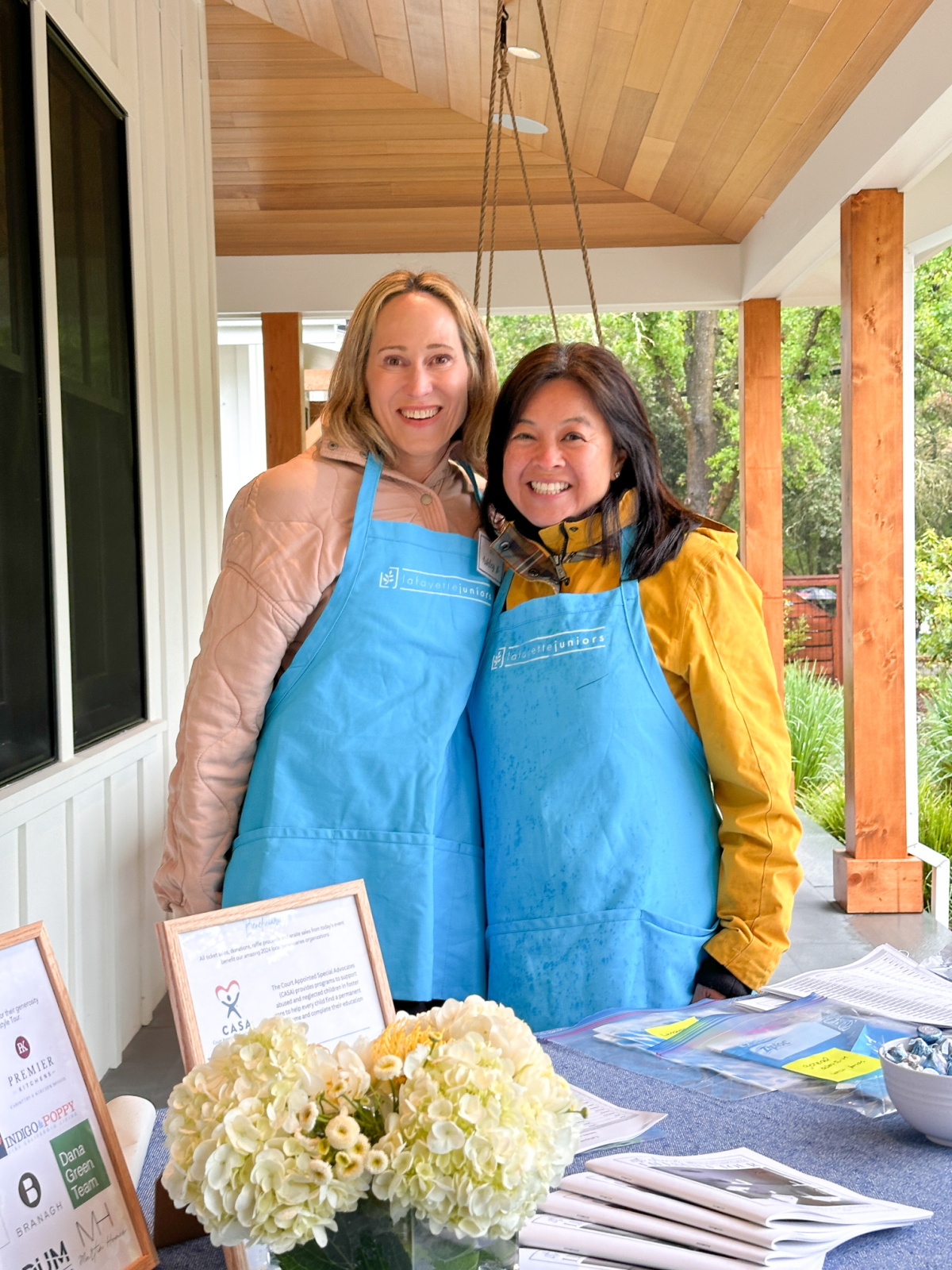 Two woman wearing blue aprons standing behind welcome at home tour.