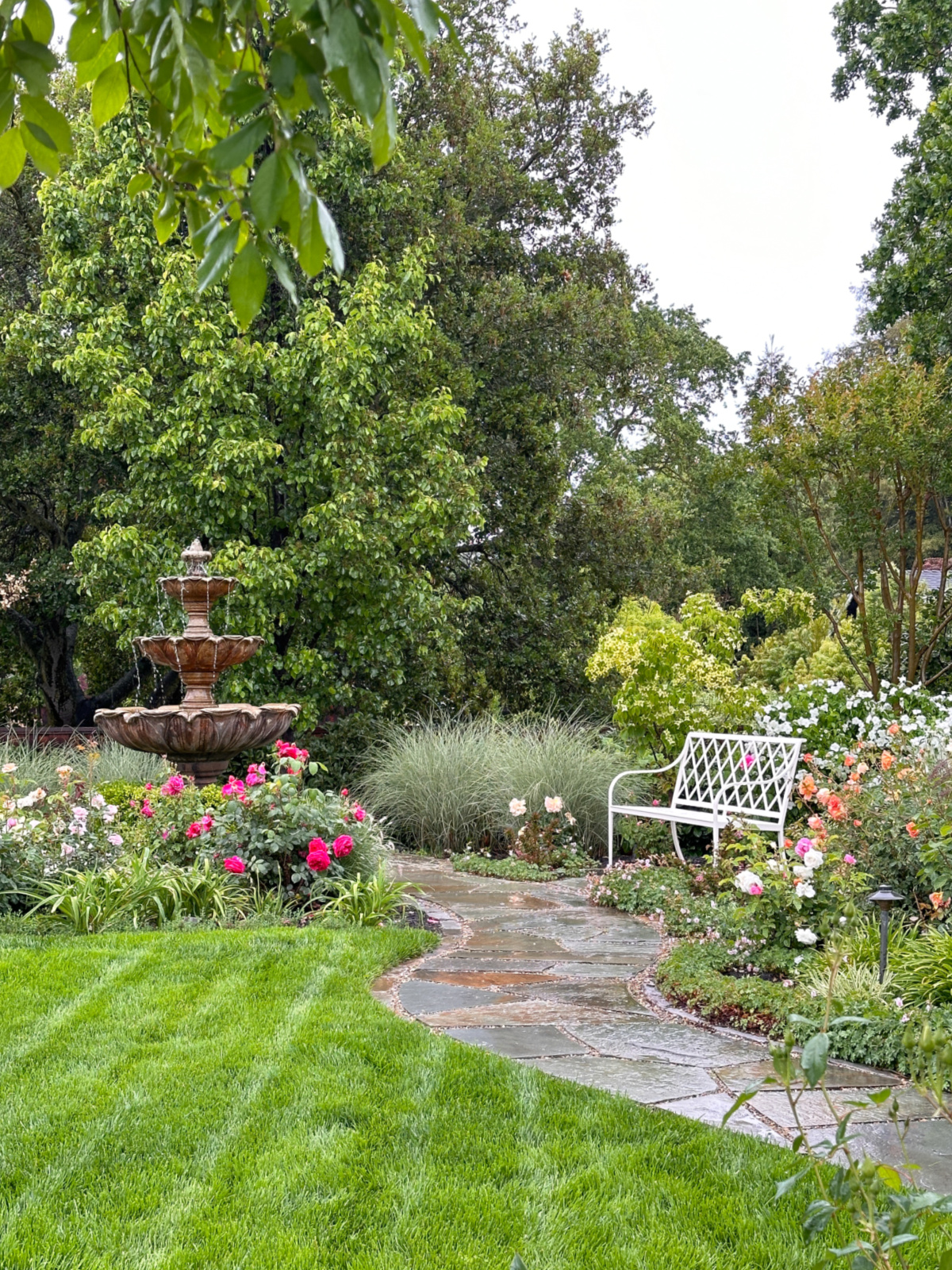 Beautiful backyard with lush lawn, fountain and white park bench.