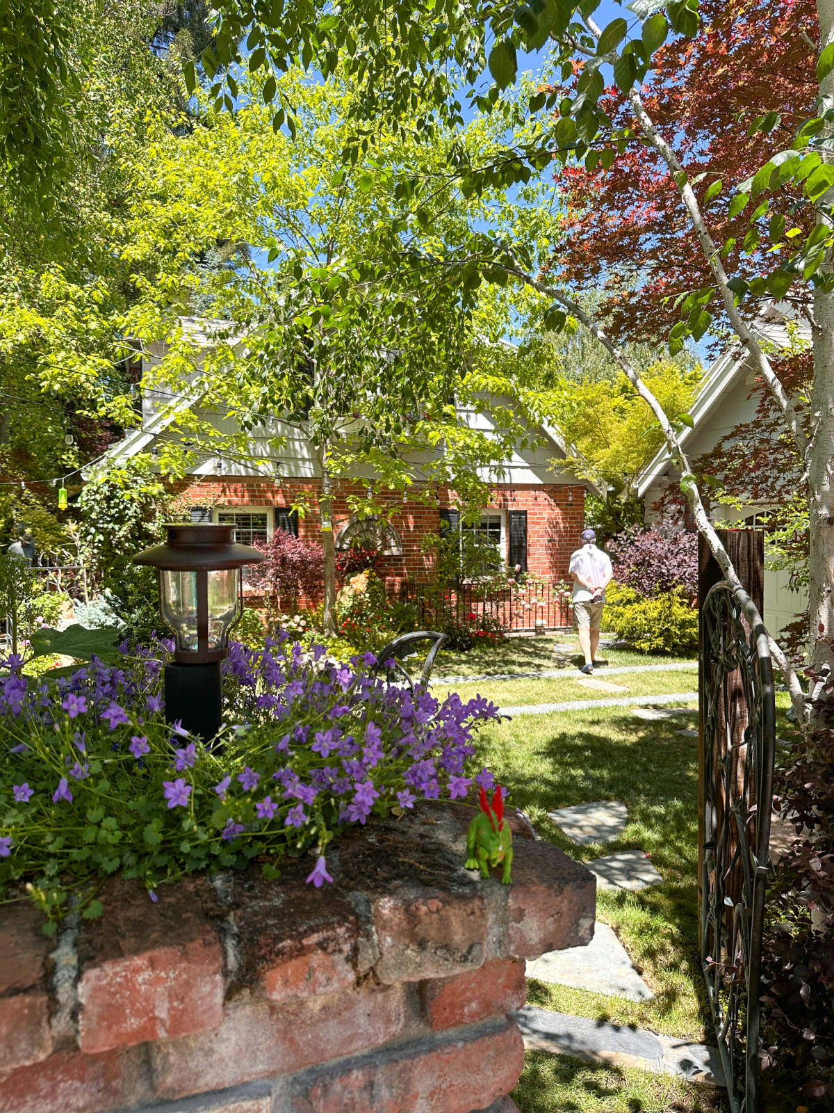 Man walking through gardens toward brick house.