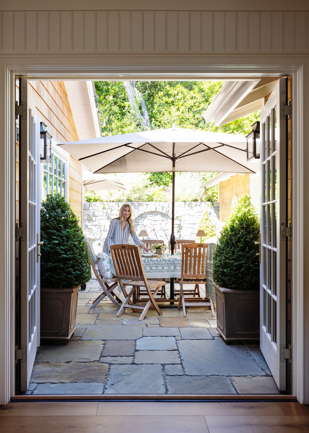 Woman standing on patio behind outdoor dining table set with green and white decor.