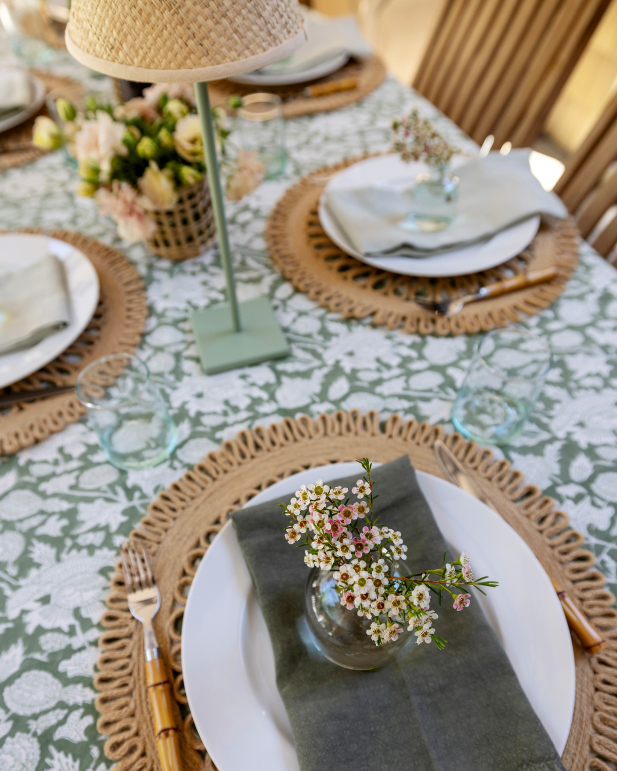 Outdoor pacesetting with small vase of flowers on top of plate and napkin.