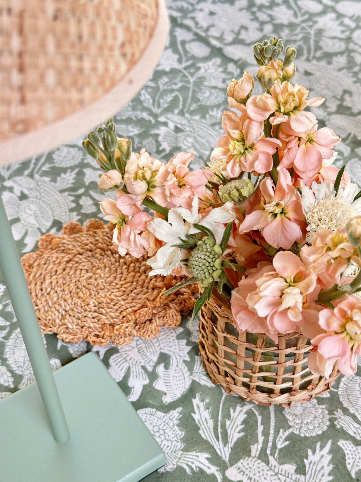 Overhead shot of outdoor table with green and white tablecloth, peach flowers in vase and top of green cordless lamp.