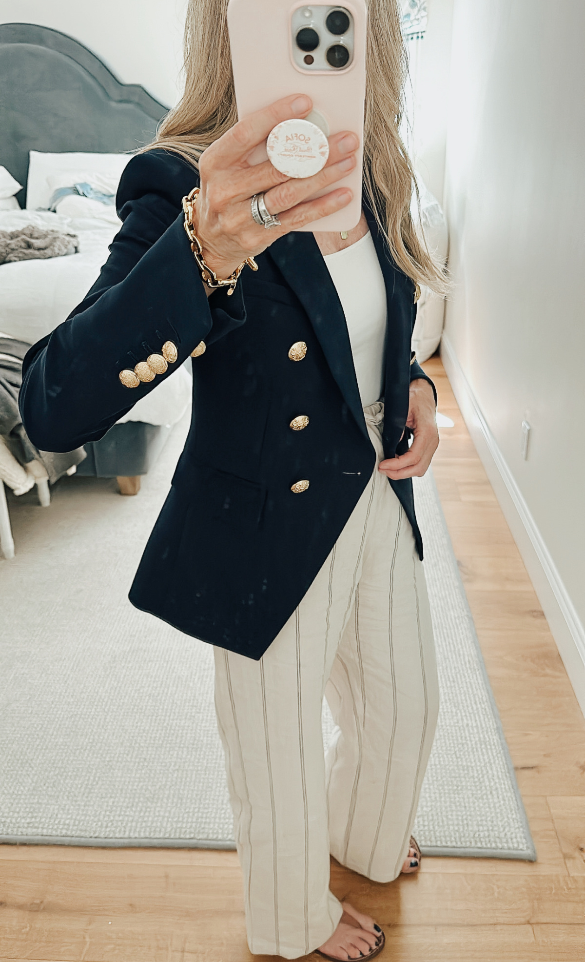 Woman taking mirror selfie wearing navy blazer, striped linen pants and sandals.