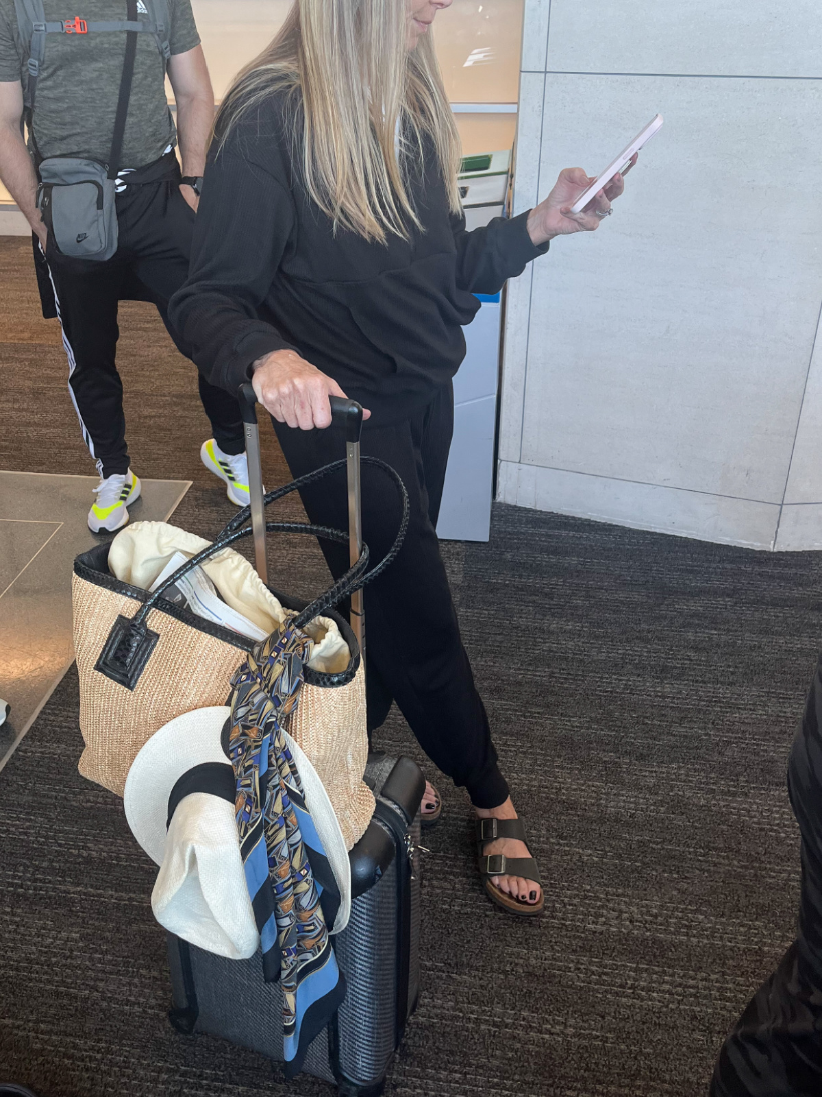 Woman wearing black jogger set next to luggage waiting to board plane.