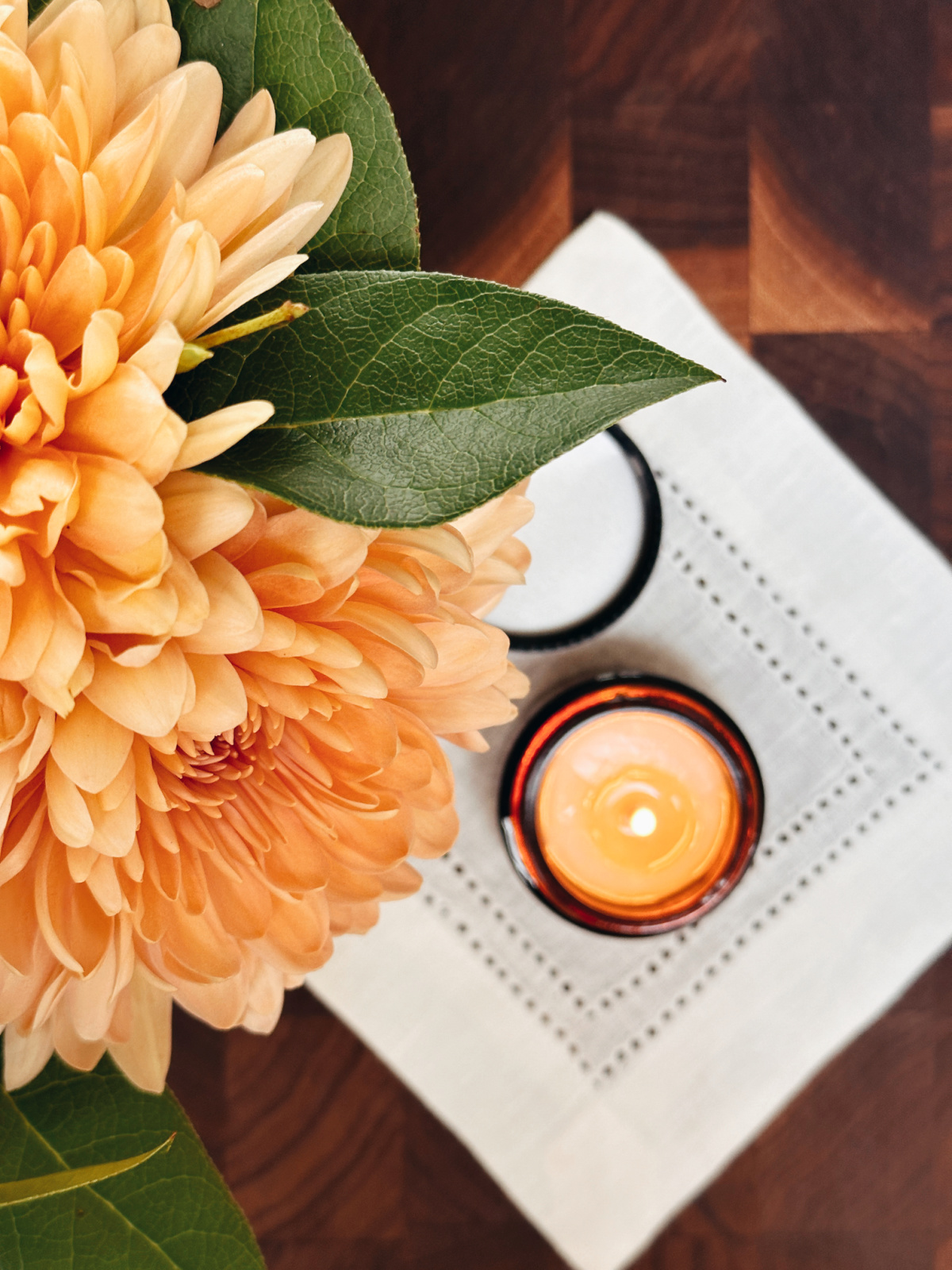 Overhead shot of flowers next to small candle burning on cocktail napkin.