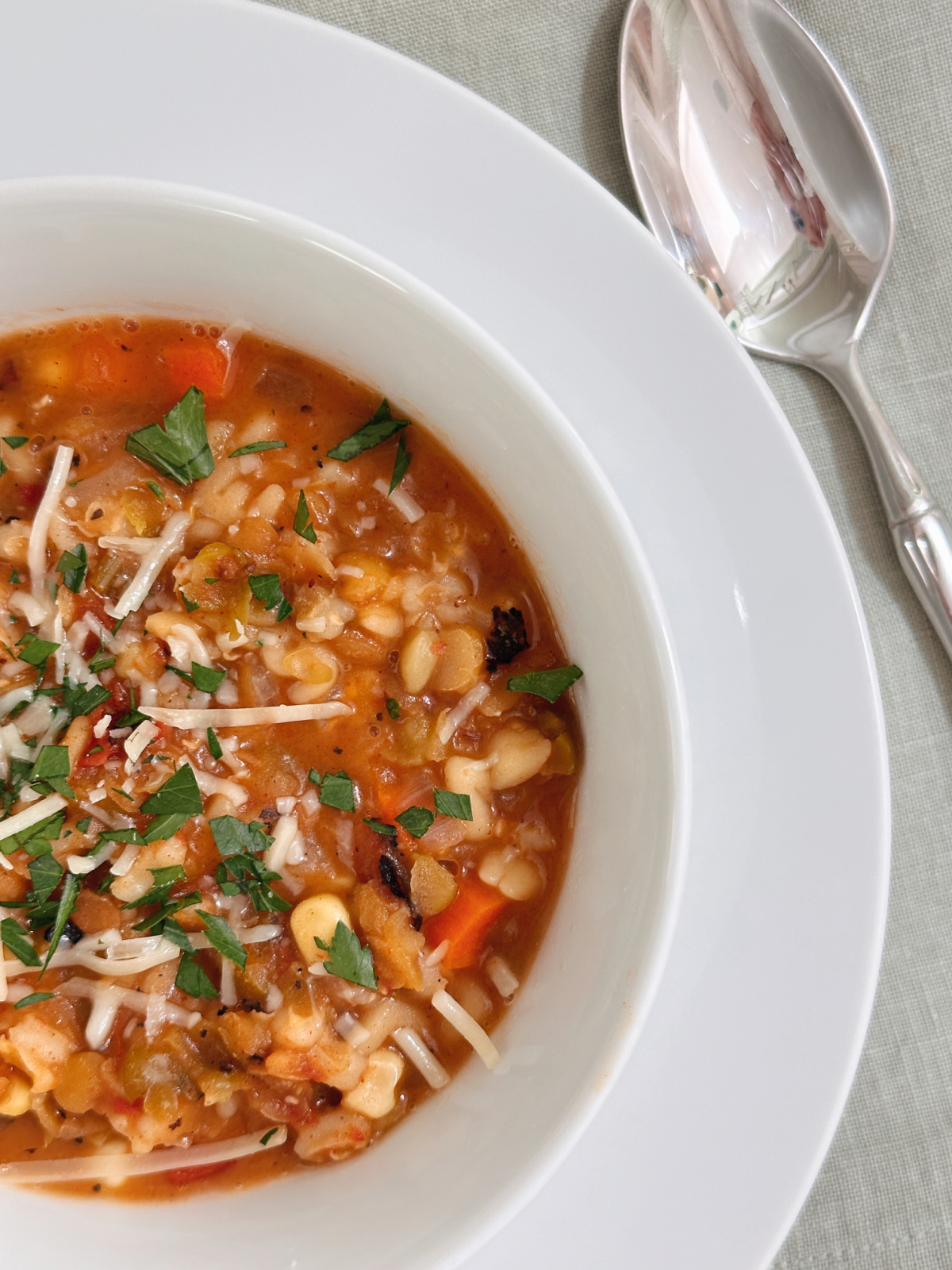 Overhead shot of bowl of vegetable soup next to green napkin and spoon.