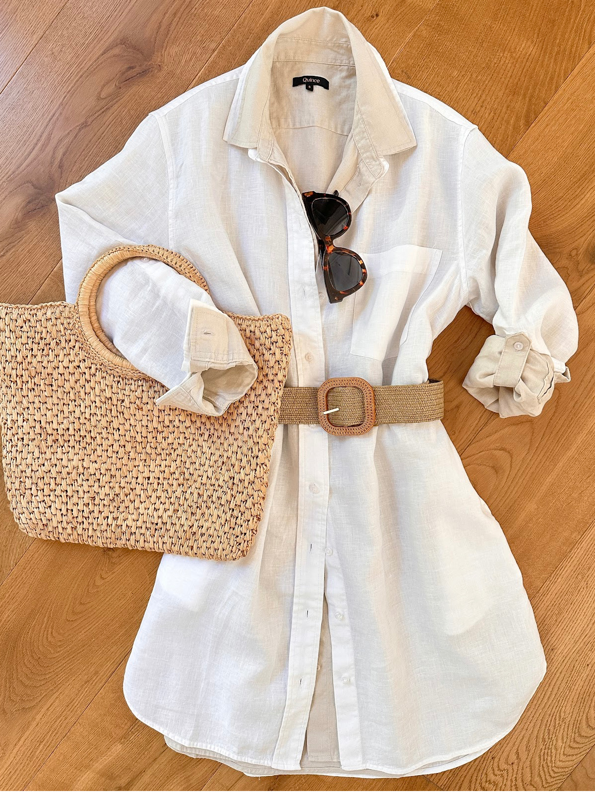 Flat lay of layered shirt dressed with belt, sunglasses and a woven bag.