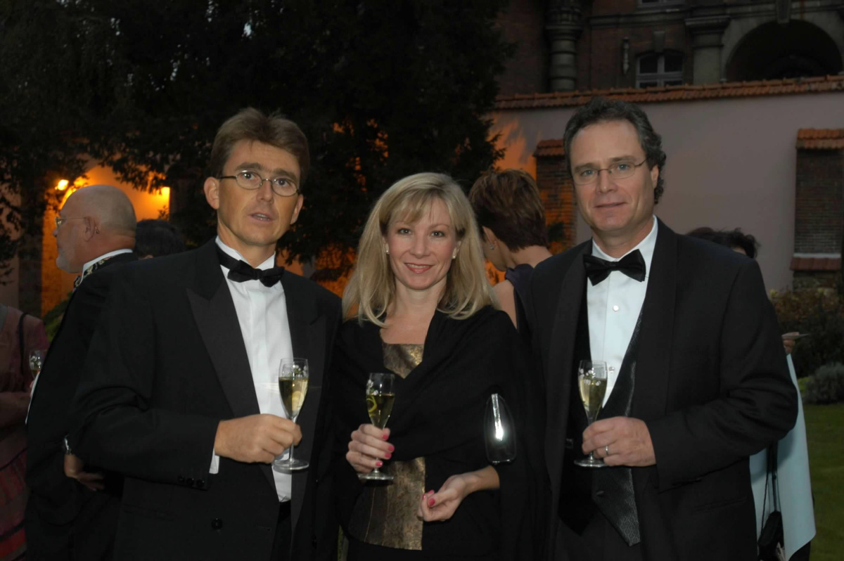 Two men and a woman holding champagne glasses in the gardens of La Maison Belle Epoque.