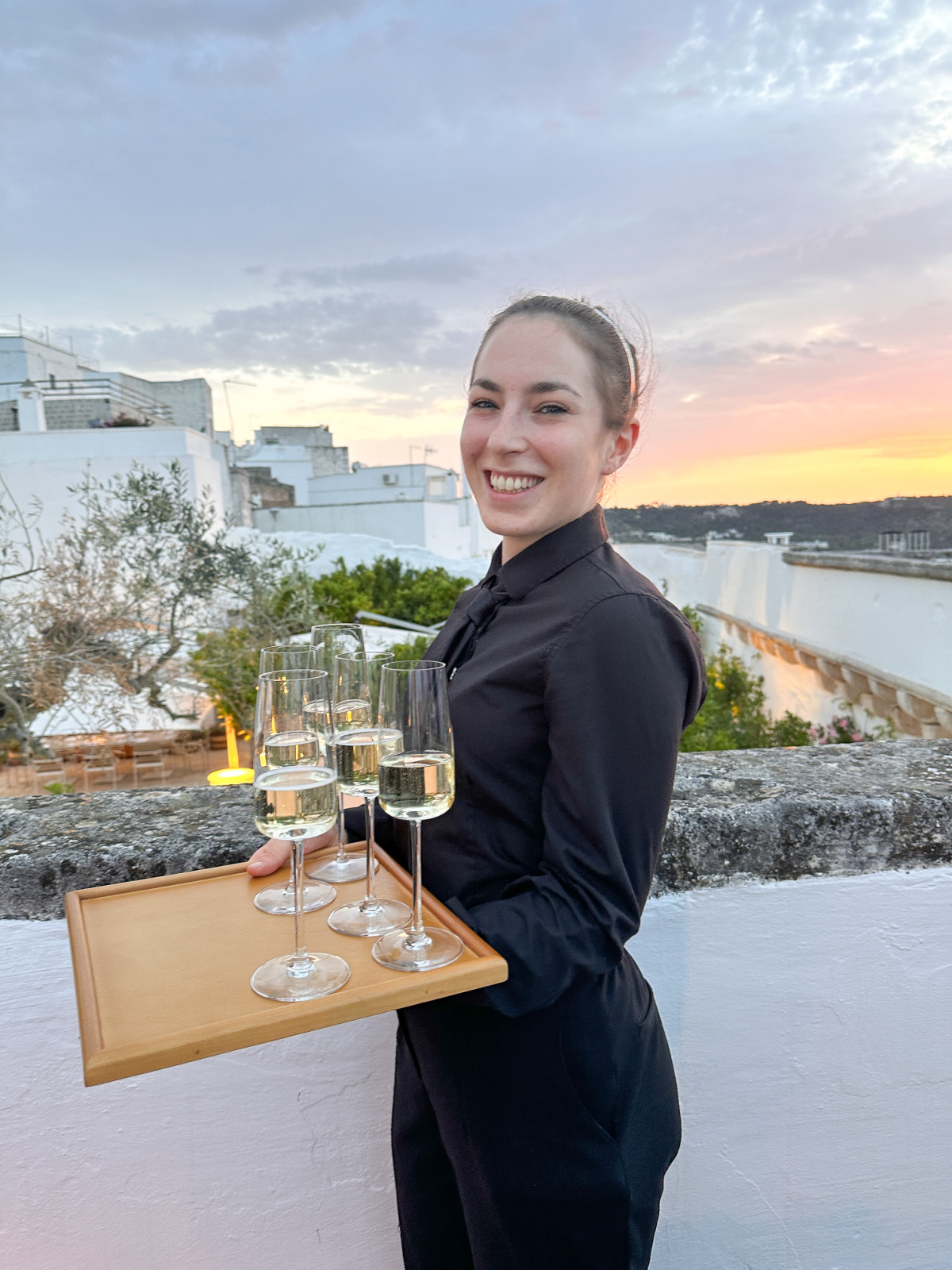Server holding tray of Prosecco on rooftop terrace in Ostuni.