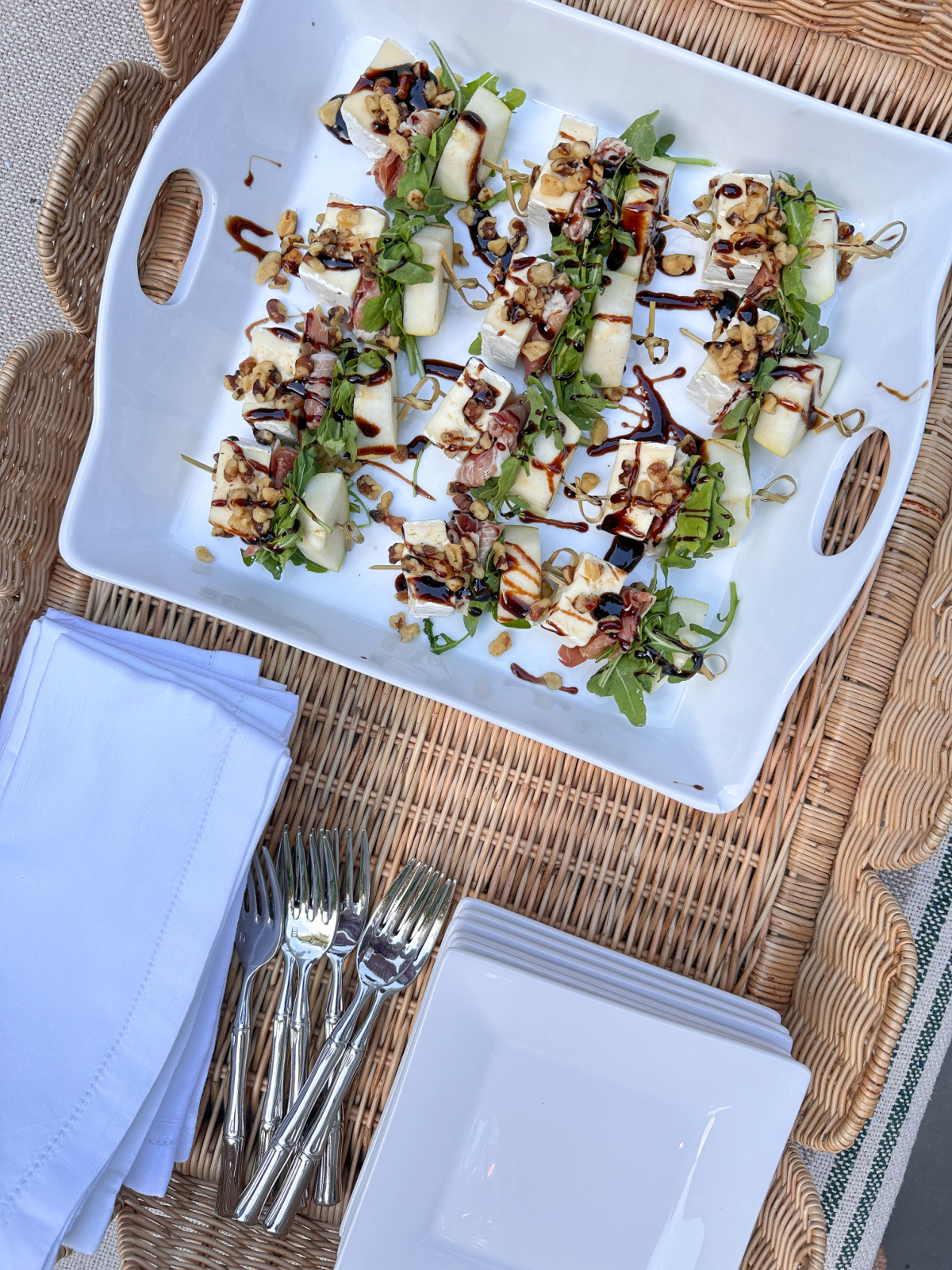 Overhead view of pear brie skewers on a white platter with napkins, small plates all in a tray.