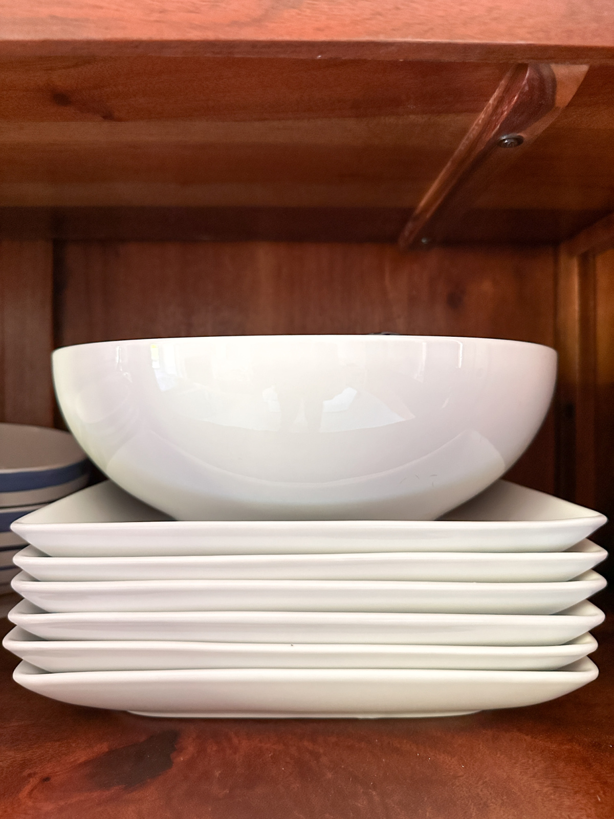 White serving platters and bowls in cupboard.
