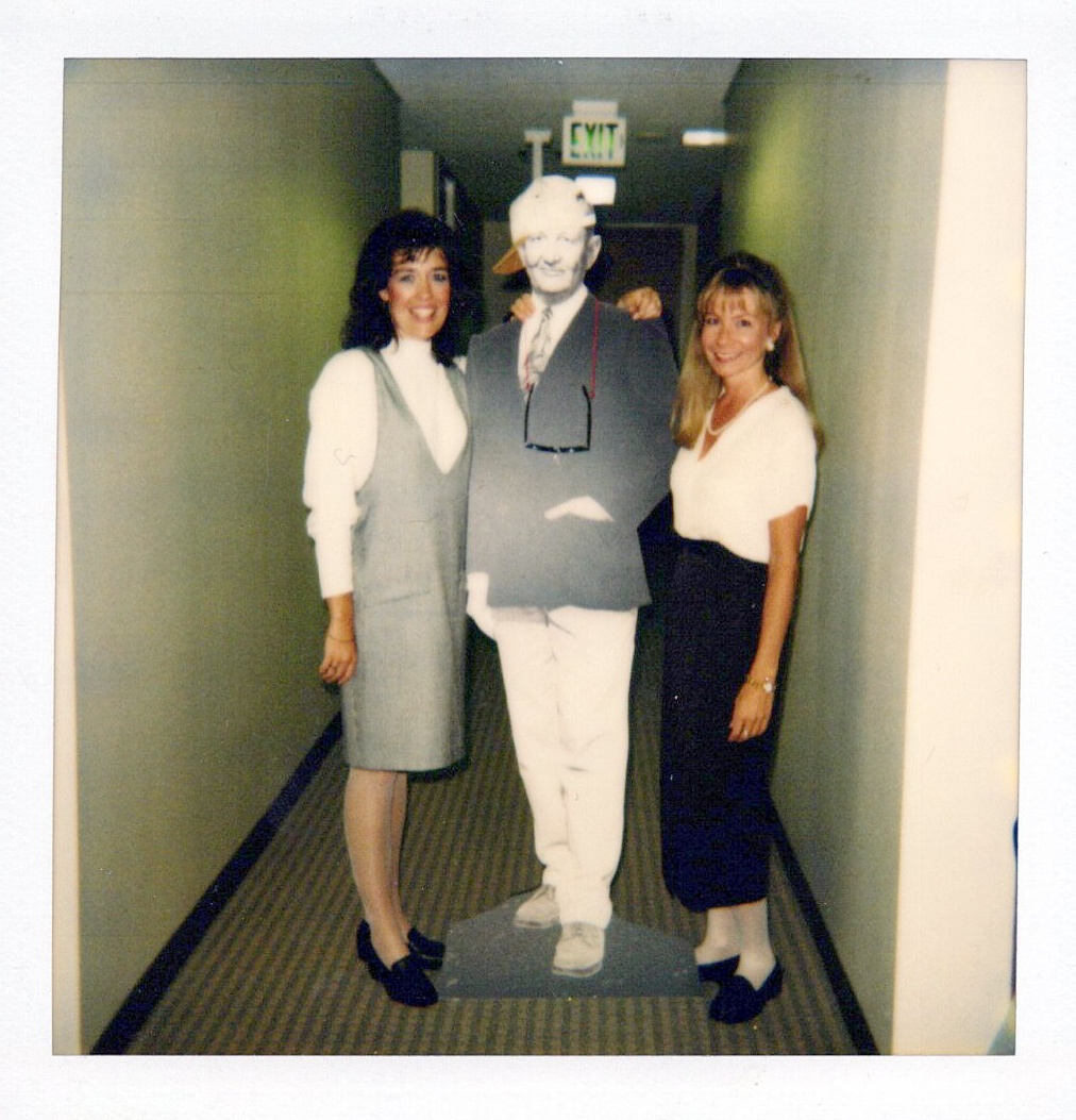 Two women posting with a cardboard cutout of Arthur Andersen in the 1990's.