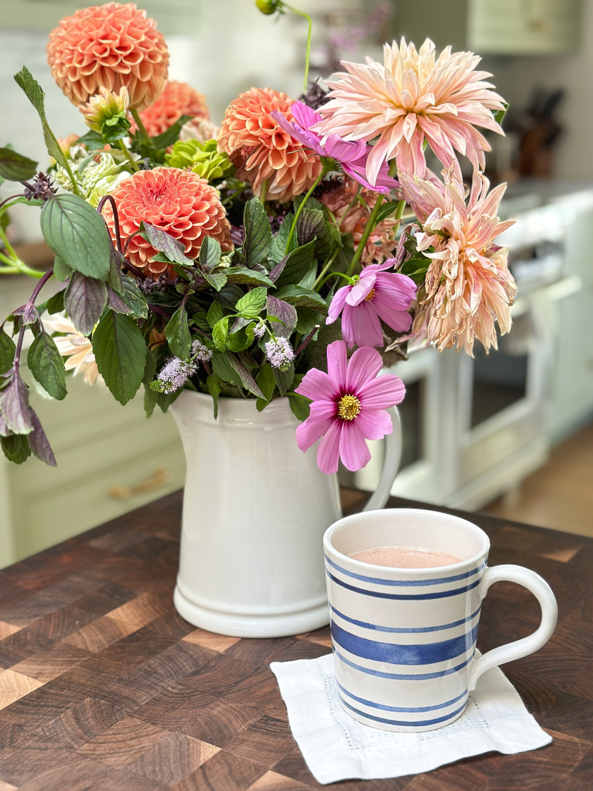 Pitcher of dahlias on island with mug of cocoa.