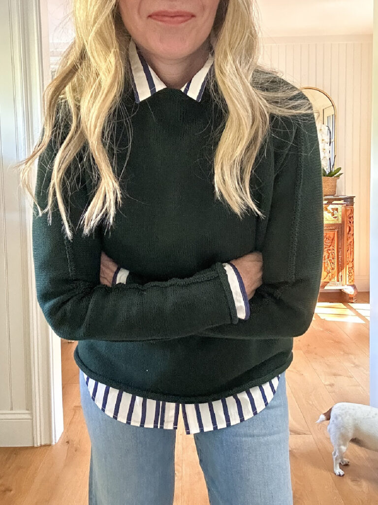 Woman wearing striped button down shirt and dark green sweater.