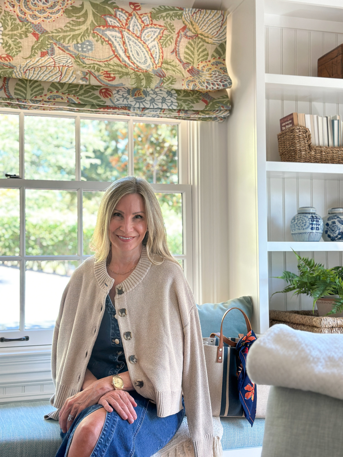 Woman sitting in window seat wearing denim dress and cardigan.