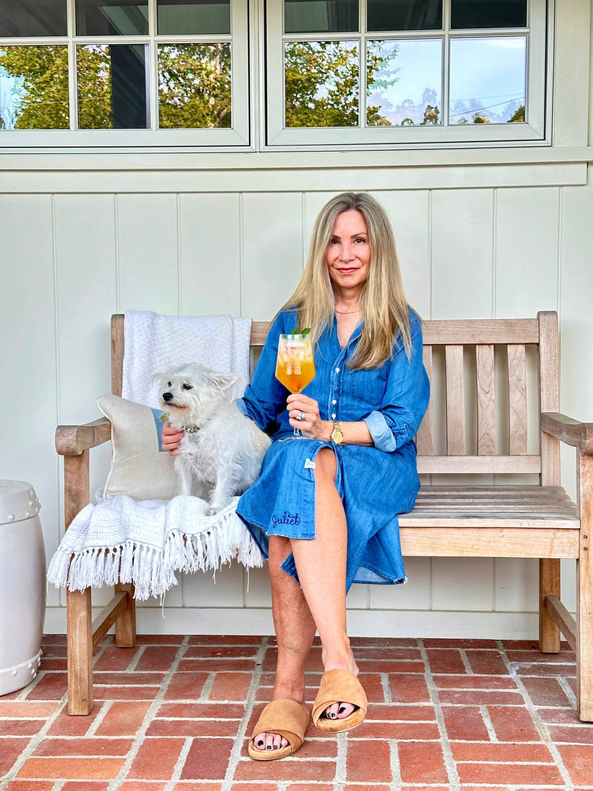Woman sitting on teak bench with small dog holding a spritzer.