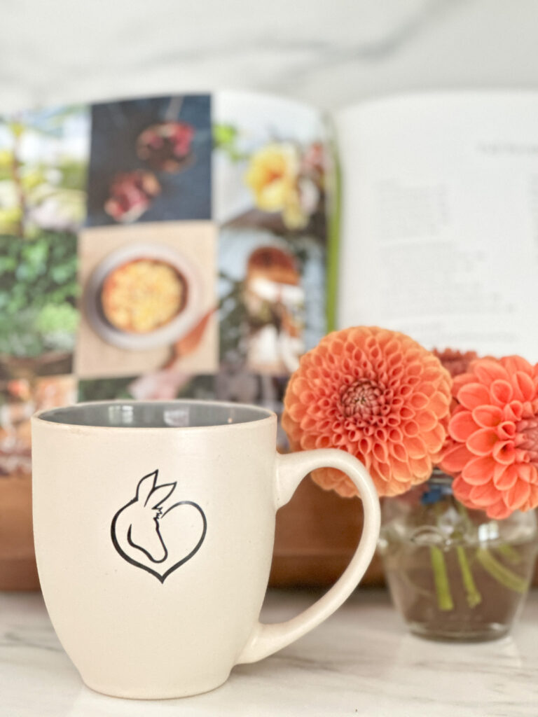 Oscar's Place coffee mug on kitchen counter next to vase of dahlias and cookbook.
