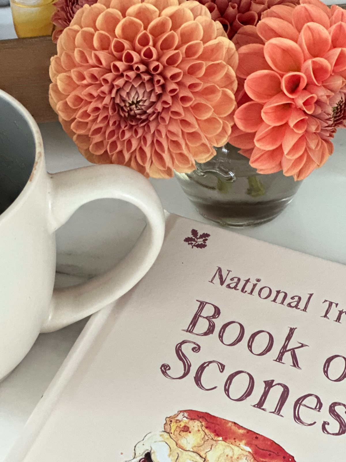 Little Book of Scones laying on counter net door a bunch of dahlias and coffee mug.