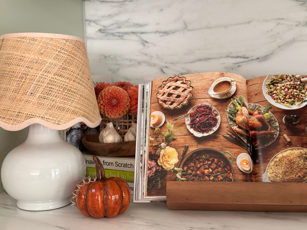 Kitchen counter lamp, pumpkin and open cookbook on rack.