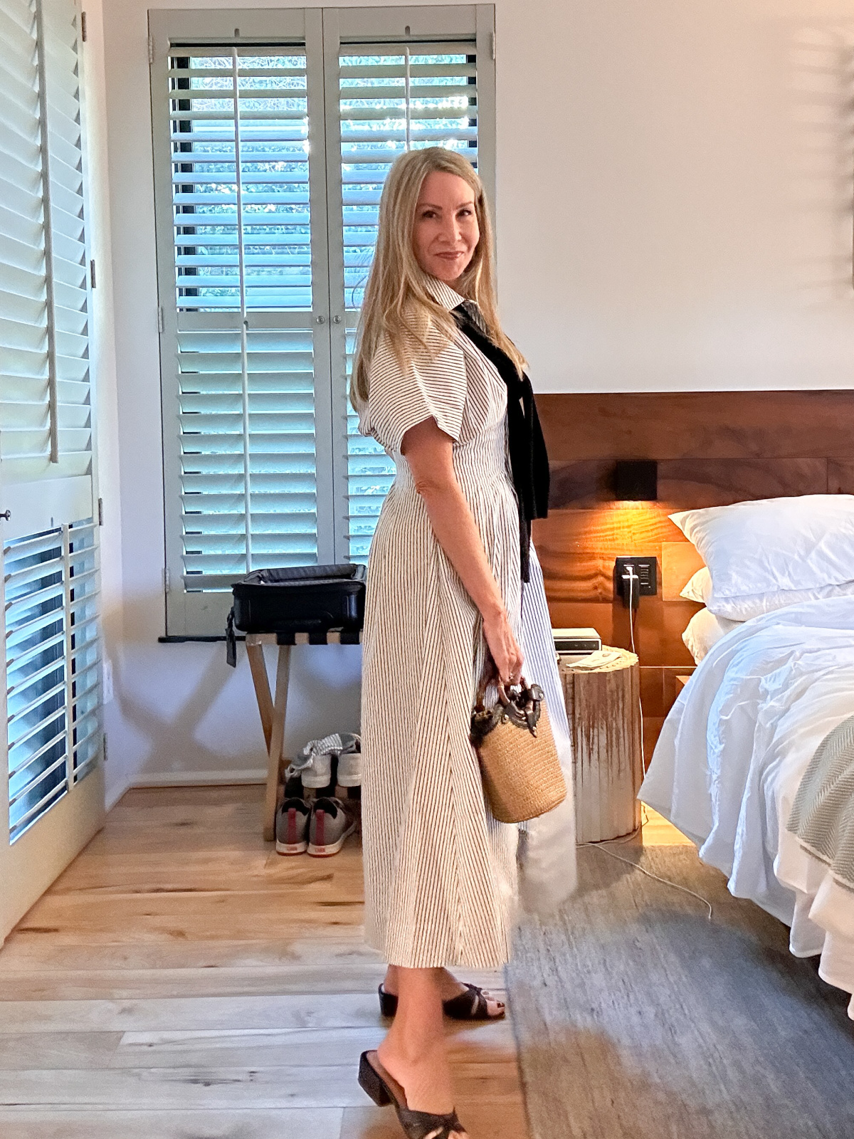 Woman wearing black and white stripe Anthropologie dress with black sweater over shoulders and woven basket bag.