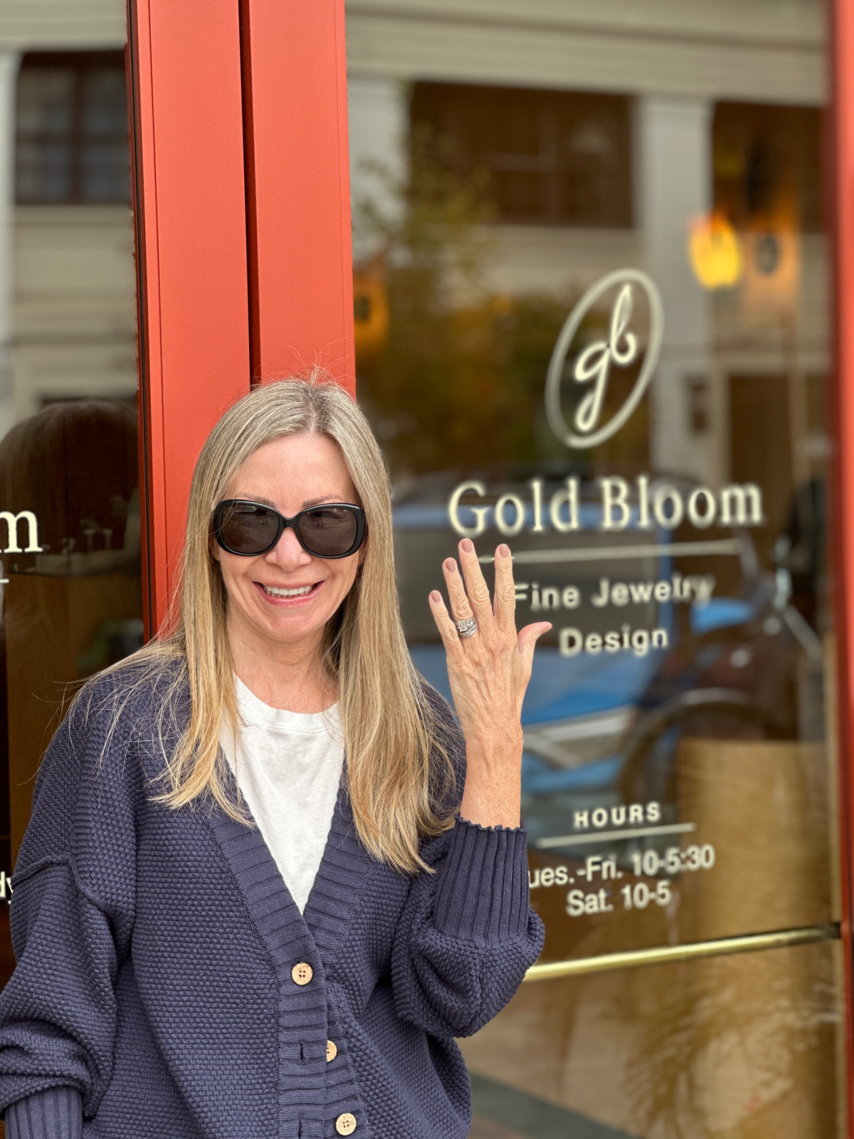 Woman showing off her engagement ring in front of Gold Bloom Jewelers.