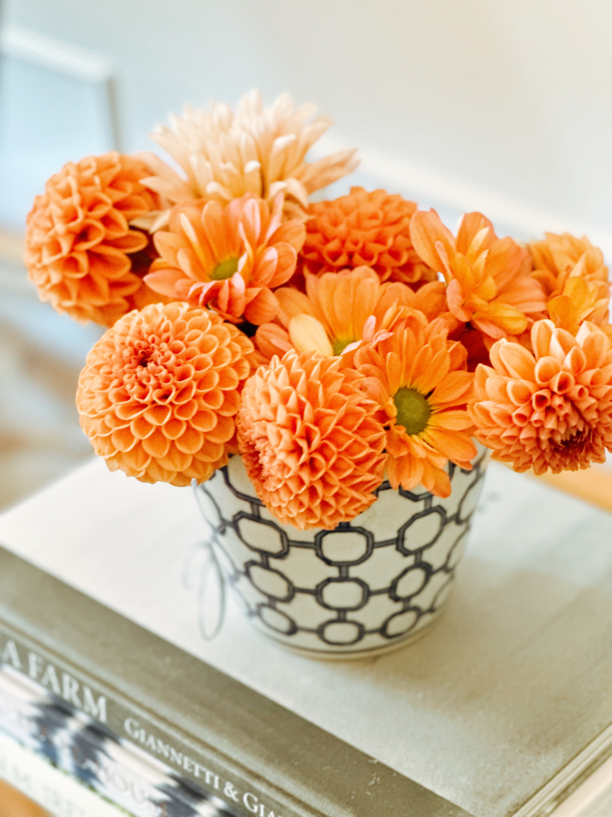 Orange dahlias in blue and white pot sitting on stack of books.