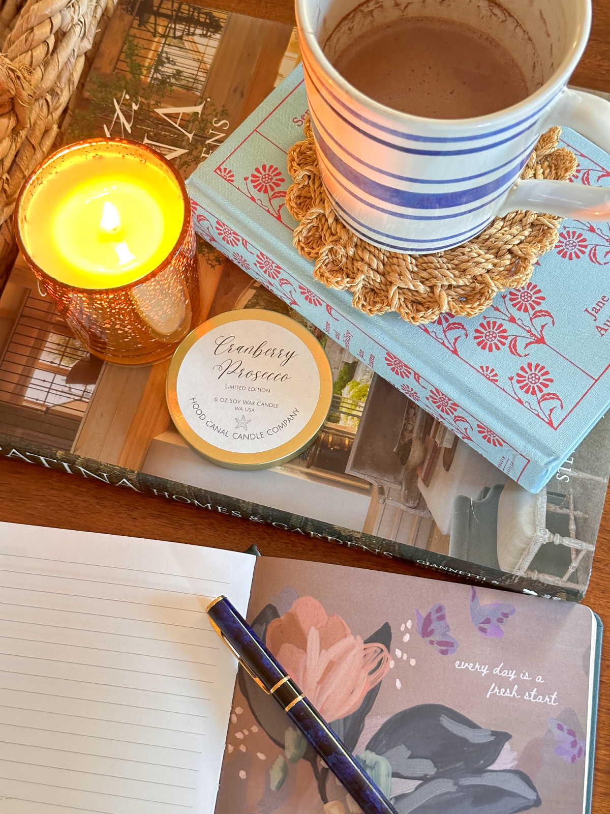 Overhead shot of journal, burning candle, books and mug of cocoa.