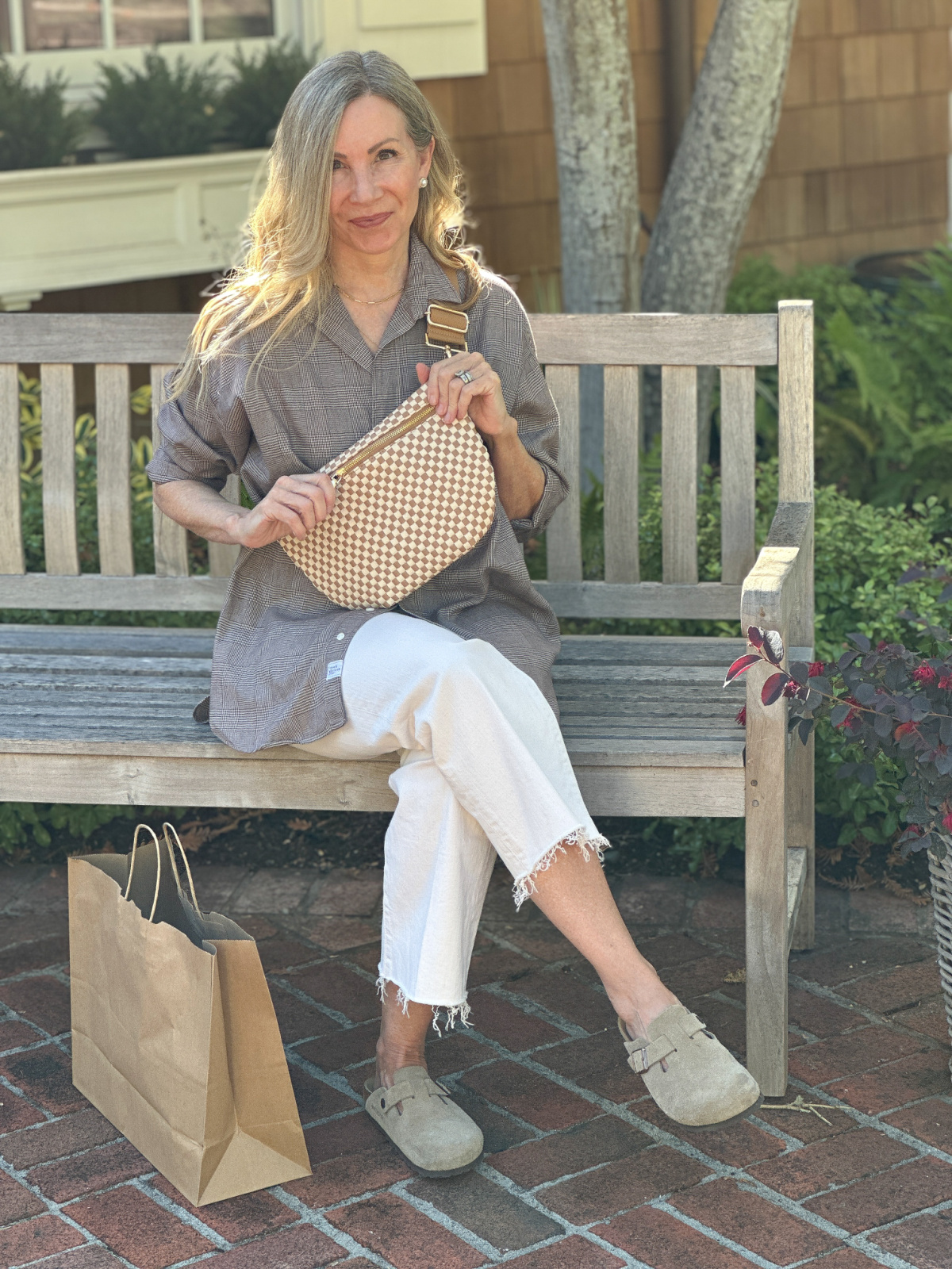 Woman sitting on bench wearing chequered cross body bag.